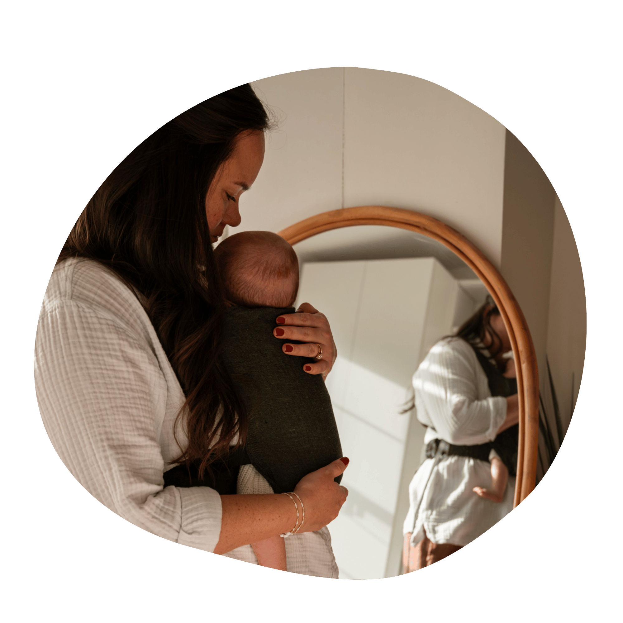 A straight size white woman stands in profile in front of a mirror. She embraces and looks down at her baby worn on her front in a Grove Sprout.