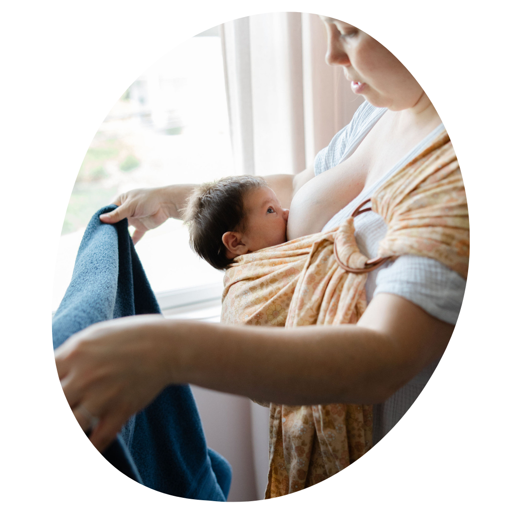 A person wears a newborn in a ring sling while nursing and folding laundry