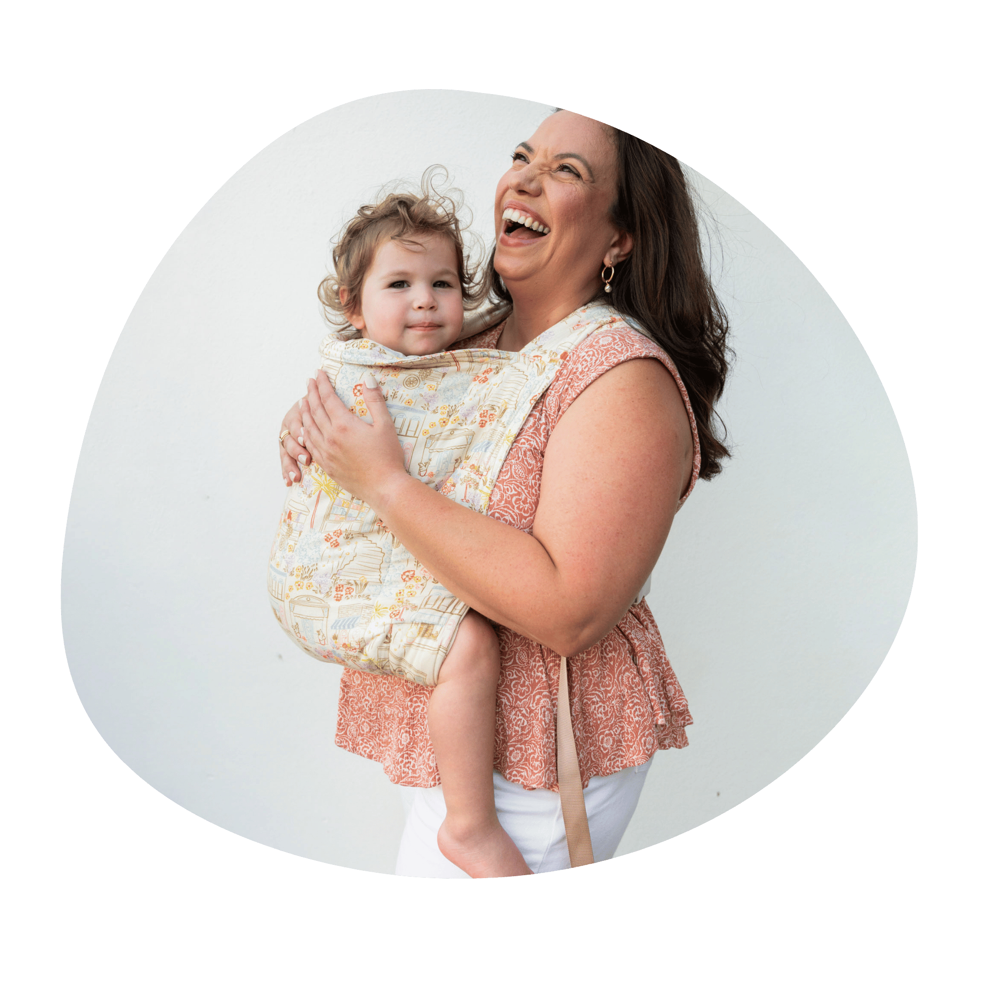 A woman wears her baby in a kid Lark on her front. She looks upward and laughs while baby looks at the camera.