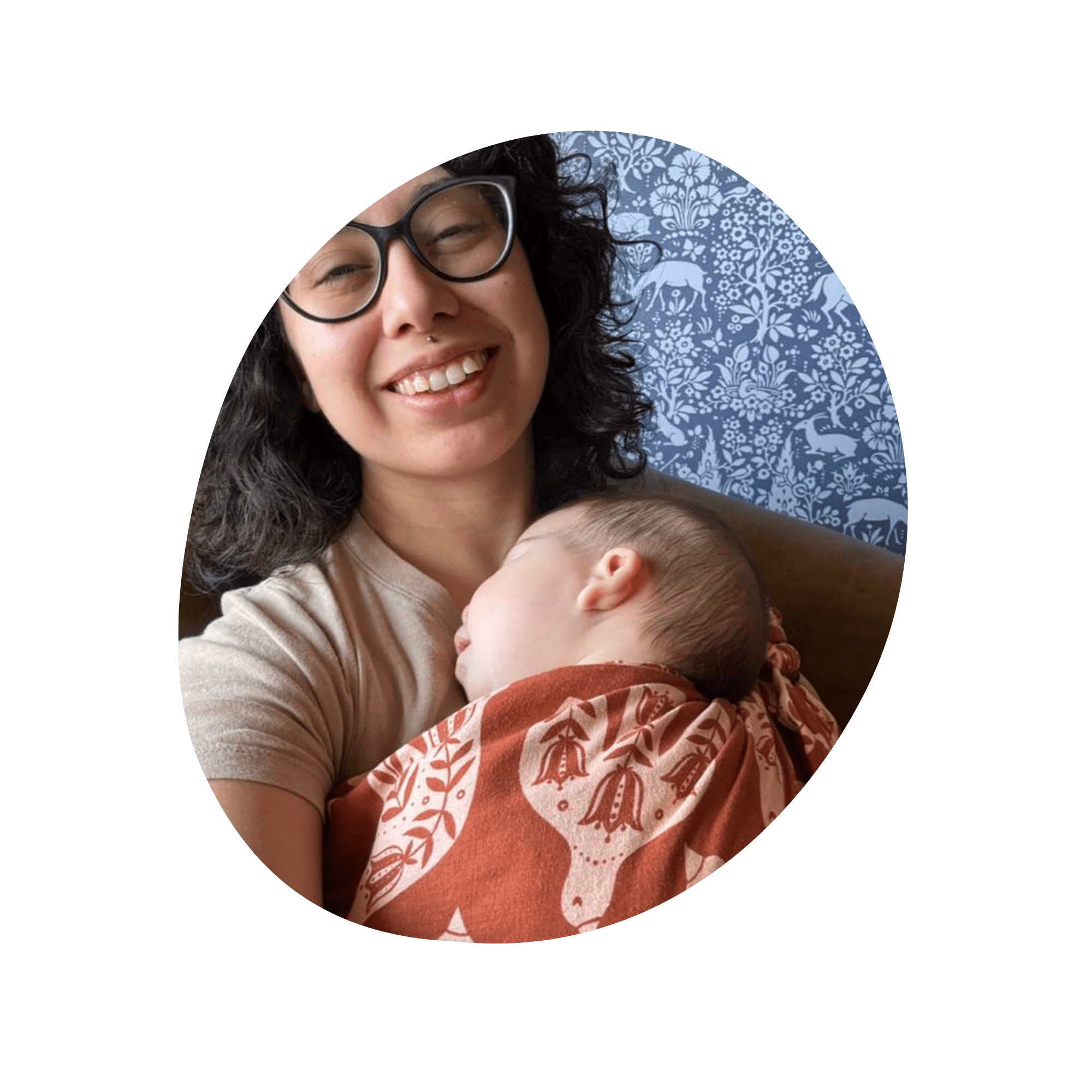 A selfie of a woman smiling at the camera while wearing a sleeping baby in a ring sling