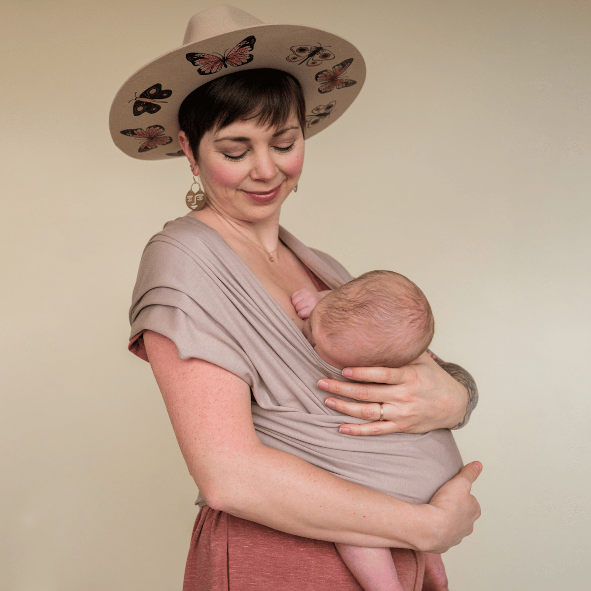 A white straight size woman nurses her baby while supporting them worn in a hope&plum fawn baby wrap