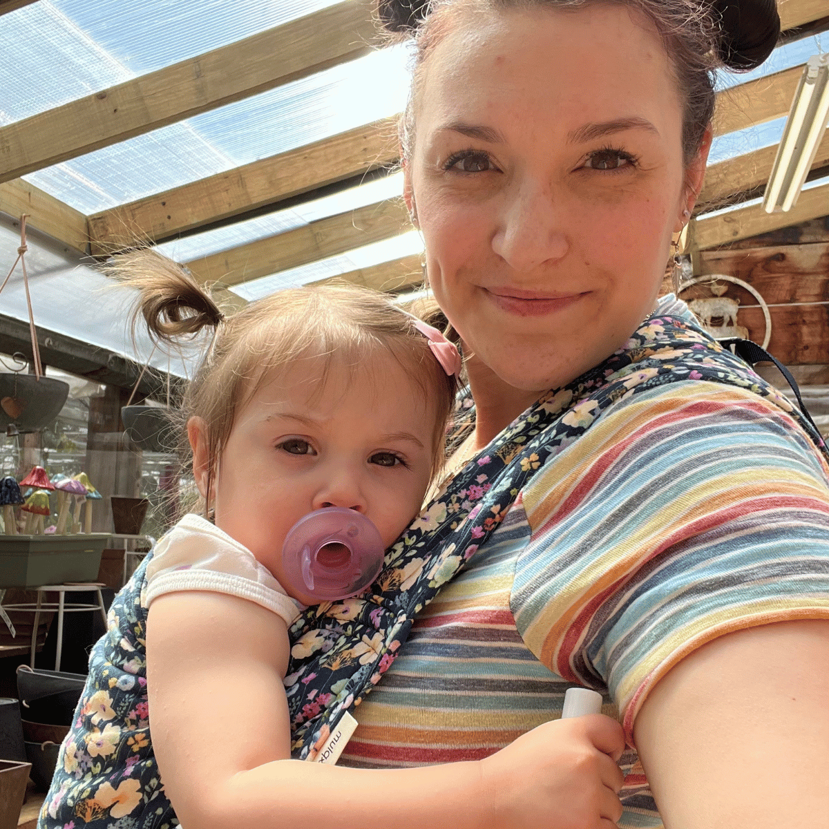 A selfie of a white straight size woman wearing her daughter on her front in an Alice Lark