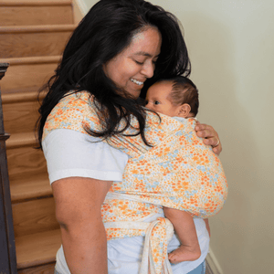 A straight size, BIPOC woman looks down and smiles at her baby, who is being carried in a stretchy wrap.