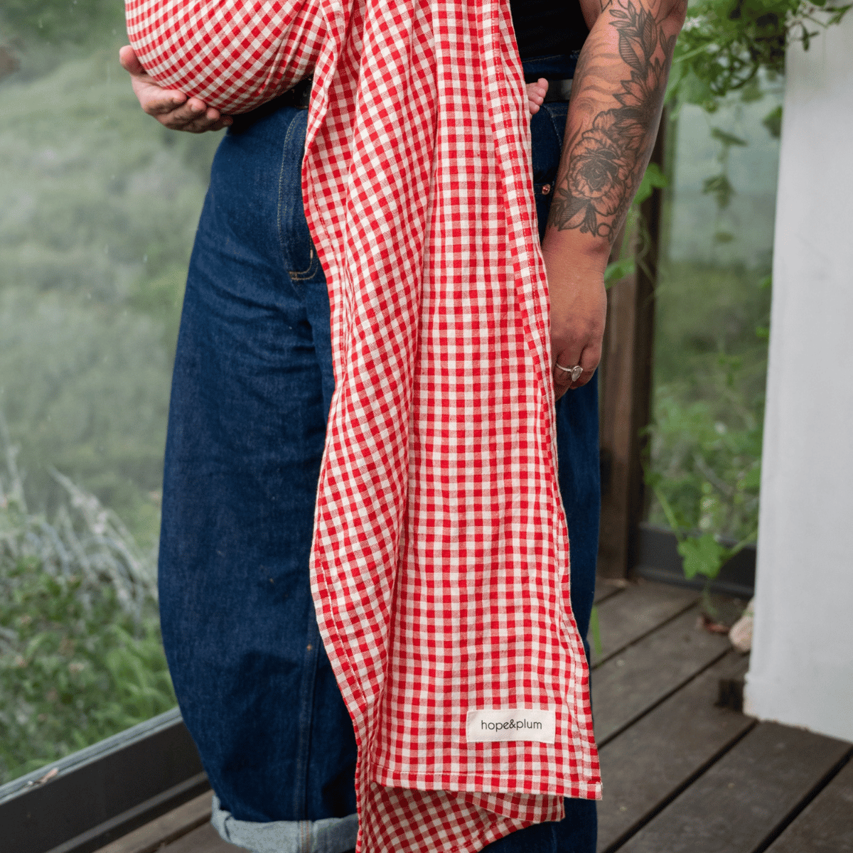 A close up on a long hope&plum ring sling tail trailing in front of a BIPOC babywearer