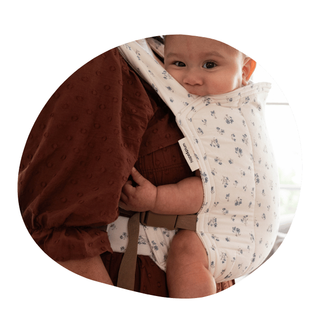 A baby smiles at the camera while worn in a front carry in a hope&plum floral Baby Lark