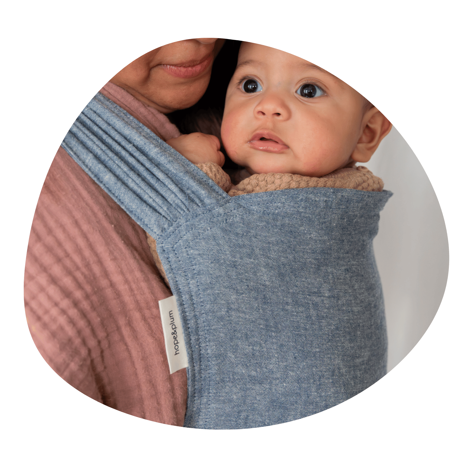 A close up of BIPOC baby worn on their caregiver's front in a Sprout.