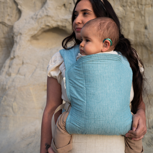Woman wearing a minimalist buckle carrier with her infant.