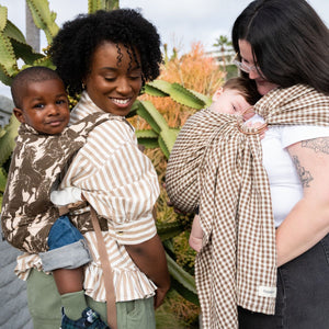 Two women, one straight-size BIPOC and the other plus-size white, wear their children in hope&plum ergonomic baby carriers