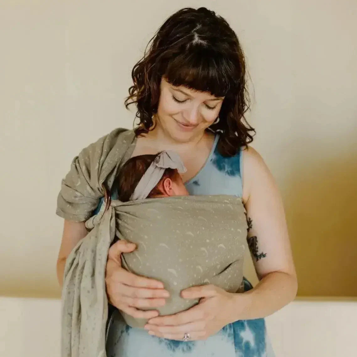 A white straight size woman wears a baby on her front in a ring sling