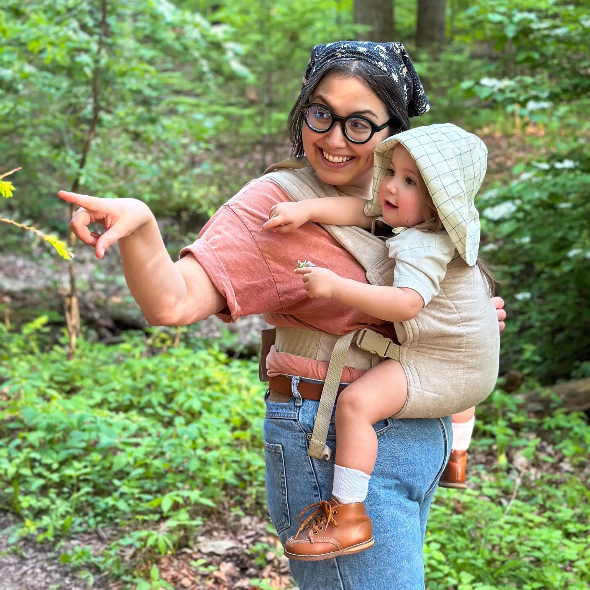 A woman babywearing a toddler in the tan Lark Baby Carrier