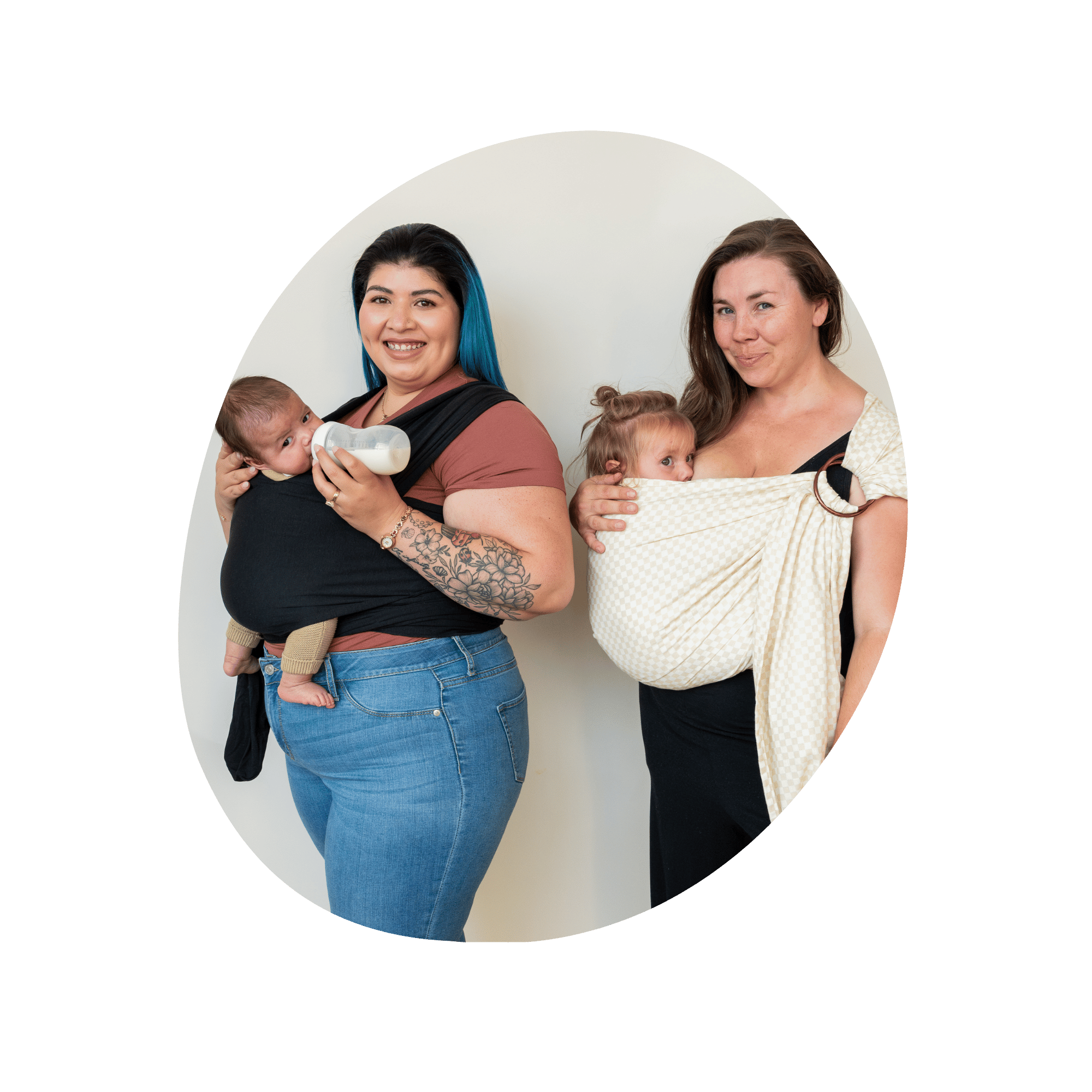 Two women stand in nearly profile. The first wears her baby in a stretchy wrap and bottle feeds. The second wears her baby in a ring sling and nurses.