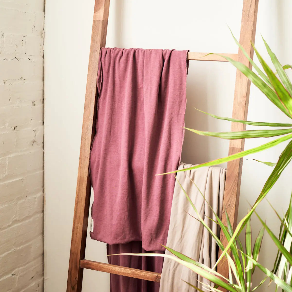 Rose colored baby wrap hanging on wood ladder next to a beige baby wrap.