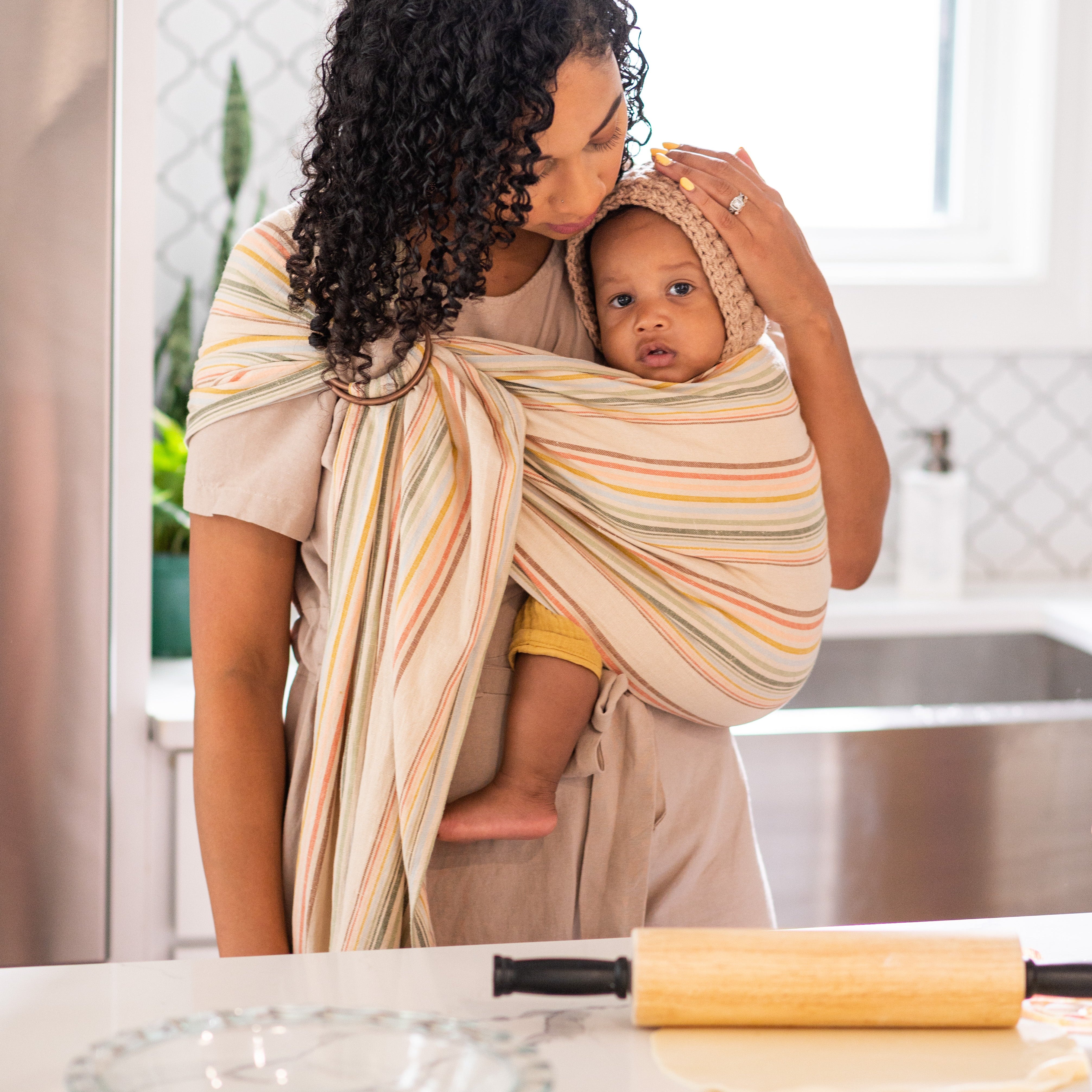 Woman holding a baby in a sling in a kitchen