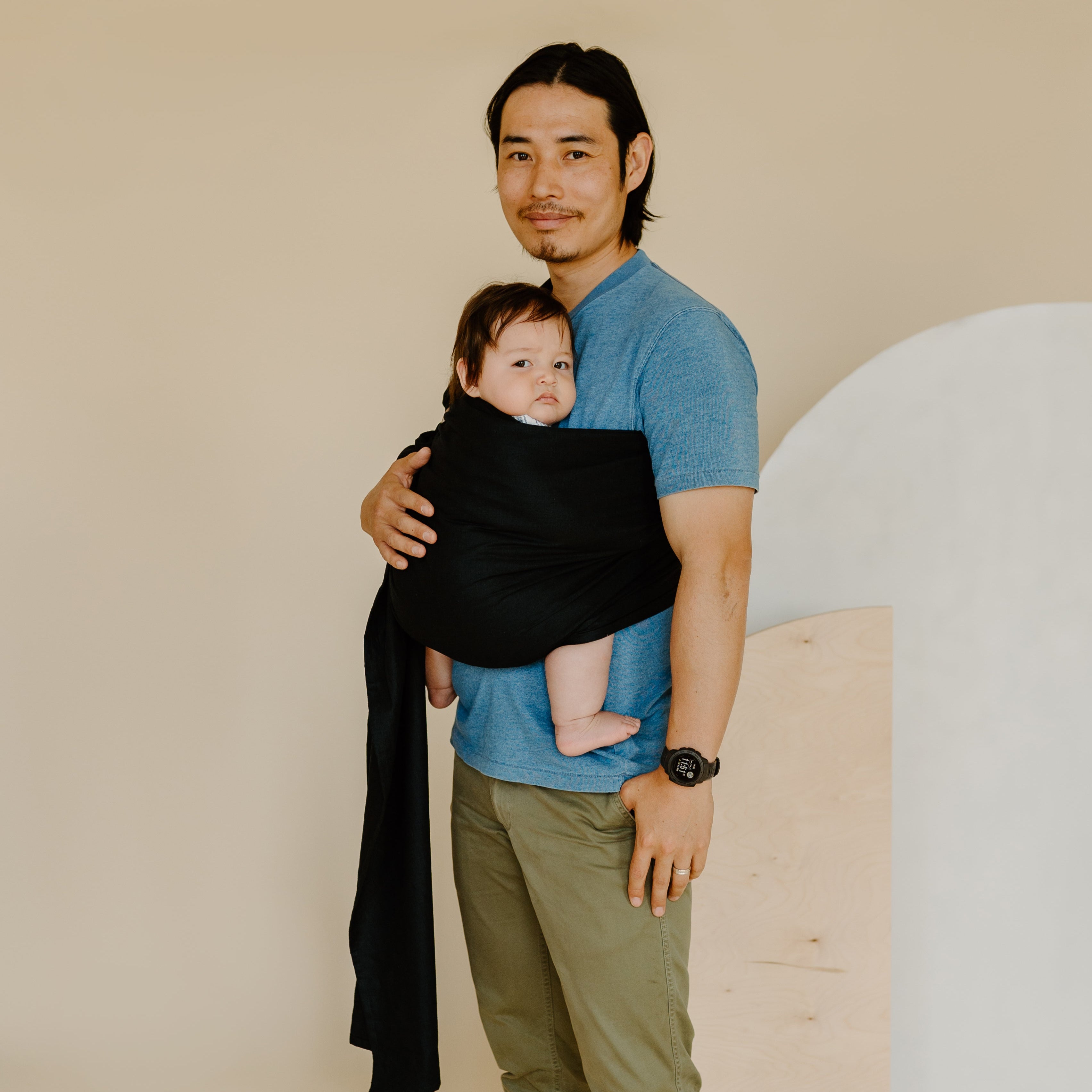 Man holding a baby in a sling against a plain background