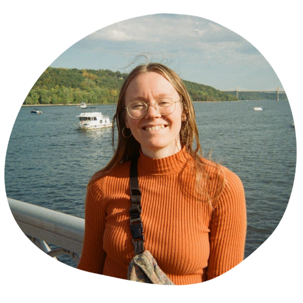 woman with brown hair, glasses, and an orange shirt standing in front of a body of water