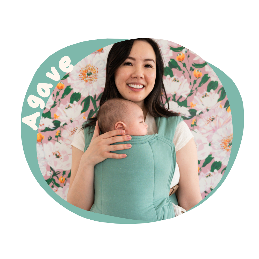 Woman holding a baby in a green baby carrier with a floral background and 'Agave' branding.