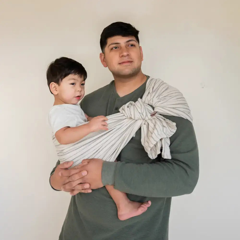 Father wearing white and black stripe ring sling baby carrier on his hip with his son.