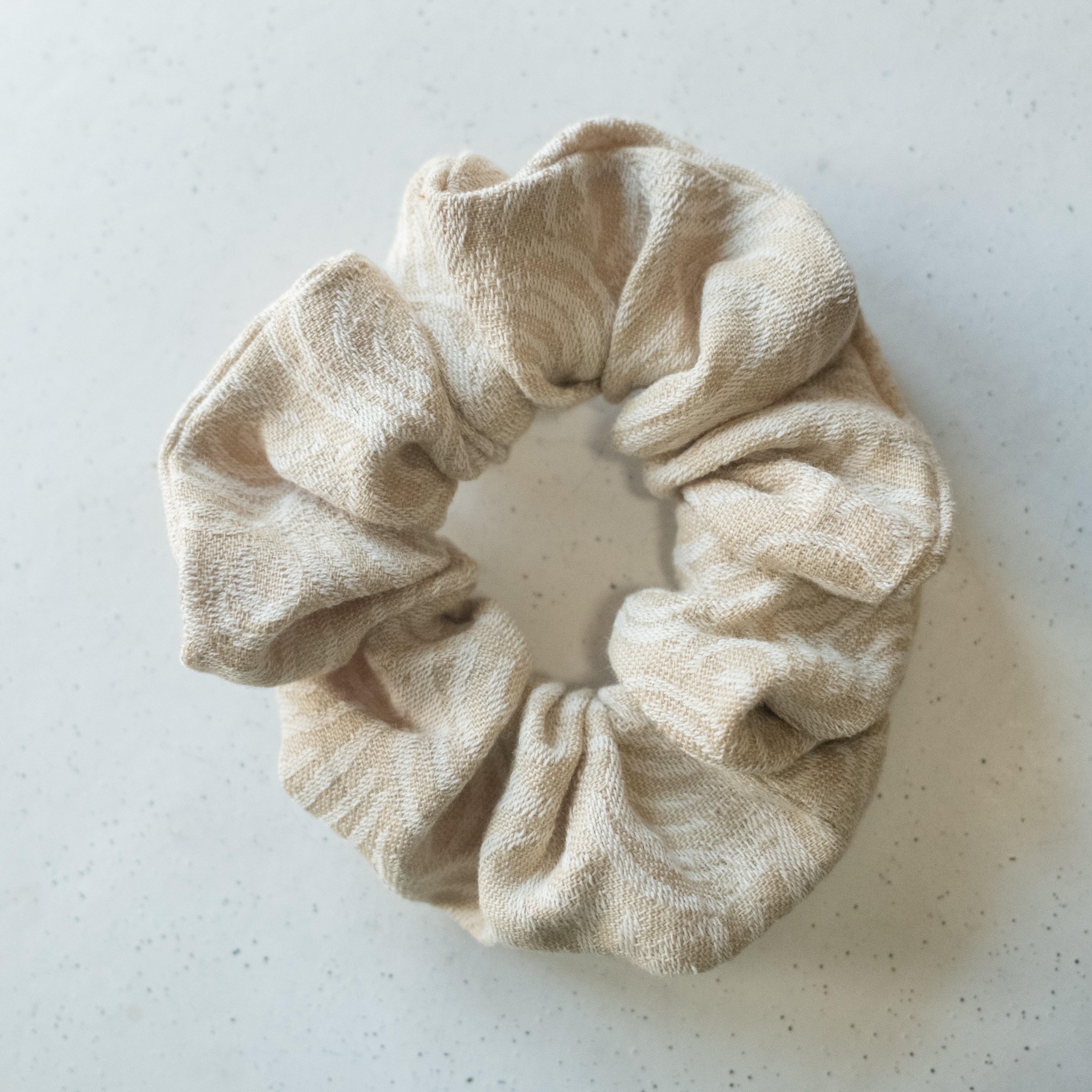 A single oversized scrunchie in a sandy beige and white wide-stripe woven fabric with a textured weave.