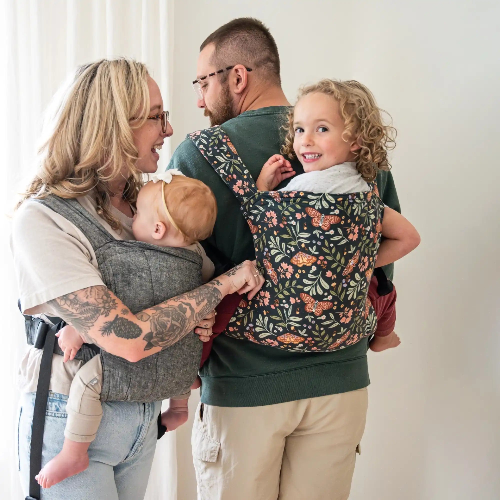 Husband and wife carrying their baby and toddler in the lark baby carrier on their front and back.