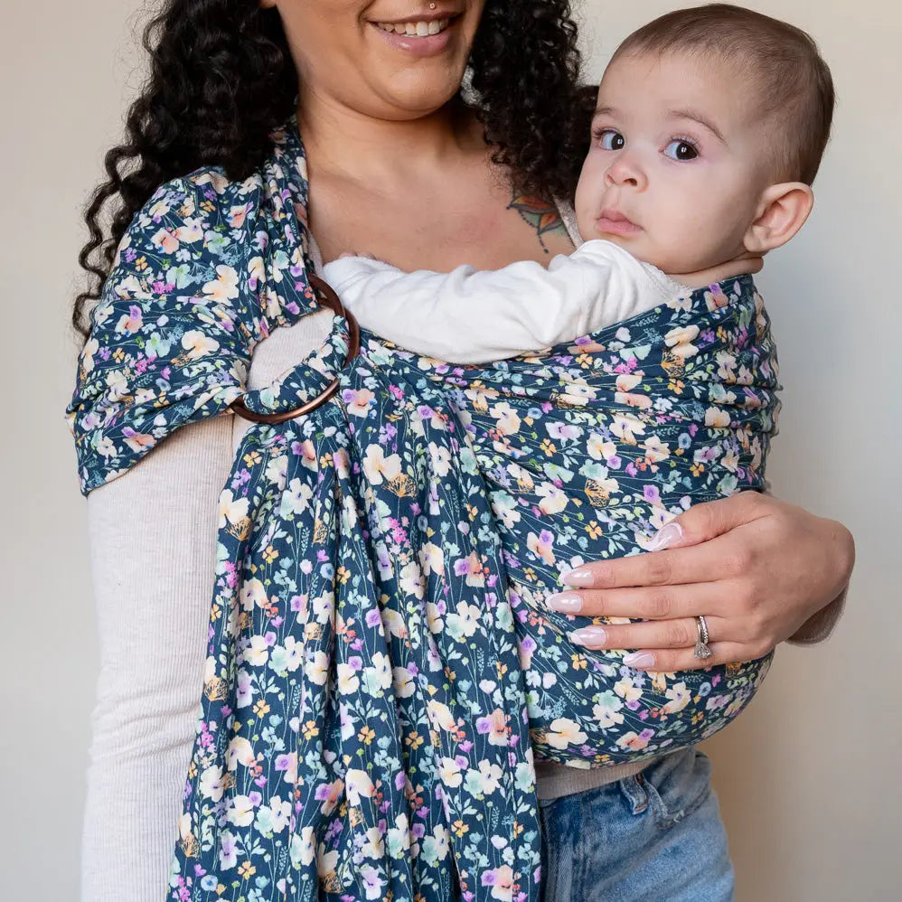 Mother wearing baby in navy floral print ring sling carrier.