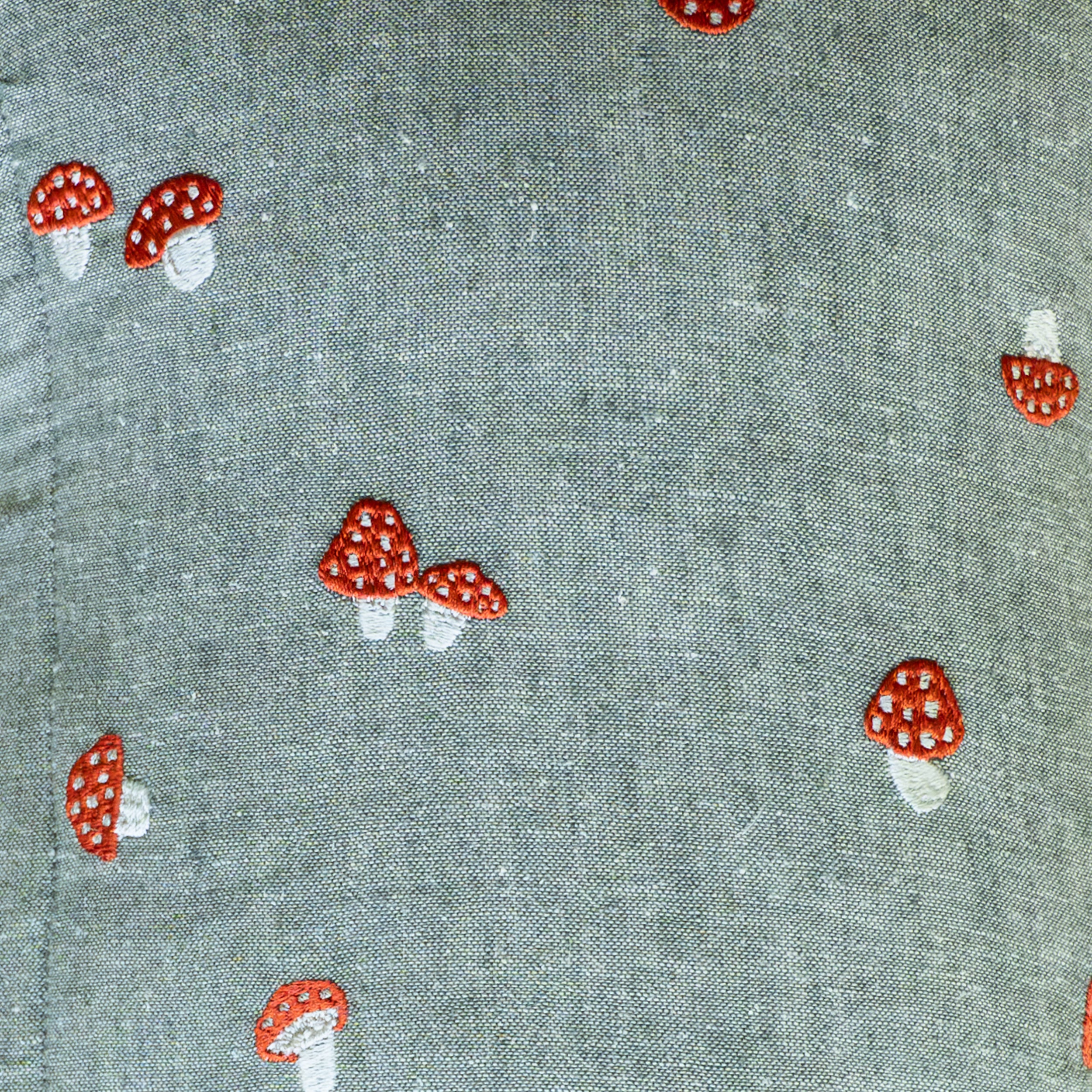 Close-up of Palm, our sage-green chambray fabric embroidered with fly agaric red and white spotted mushrooms, used in the Amanita colorway.