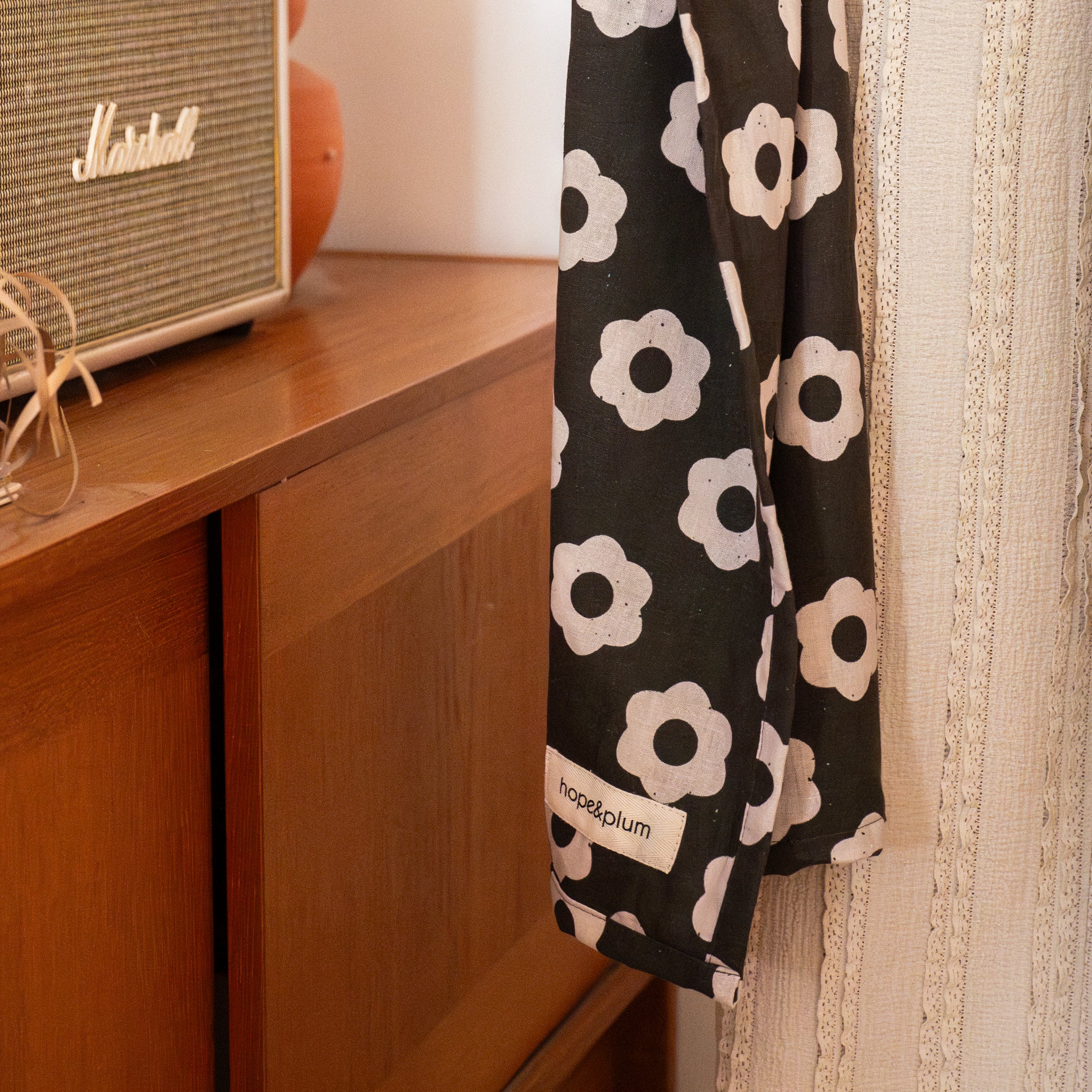 Black ring sling with white floral pattern hanging on a wooden surface next to a Marshall amplifier.