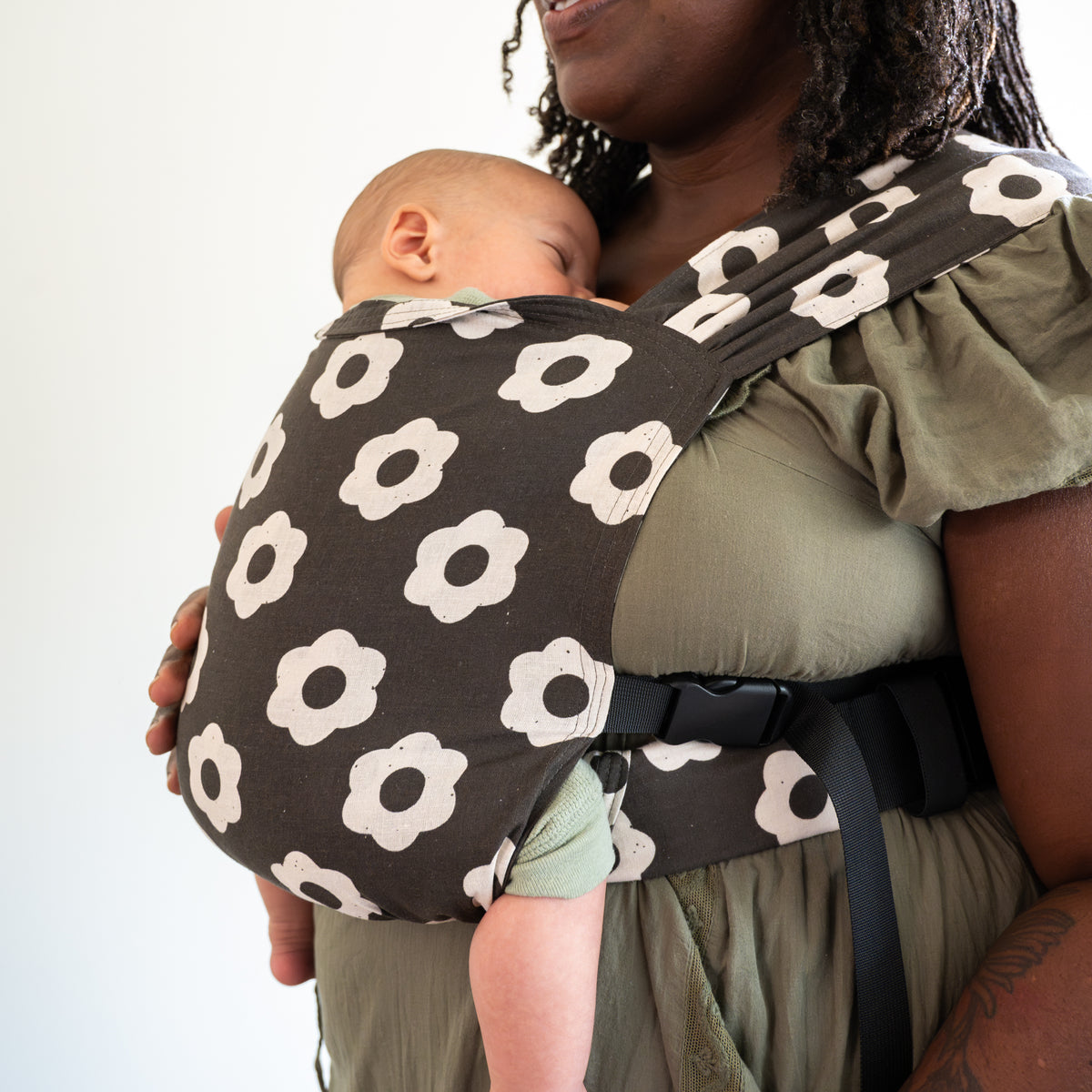 Woman holding a baby in a black and white floral-patterned newborn buckle carrier against a white background