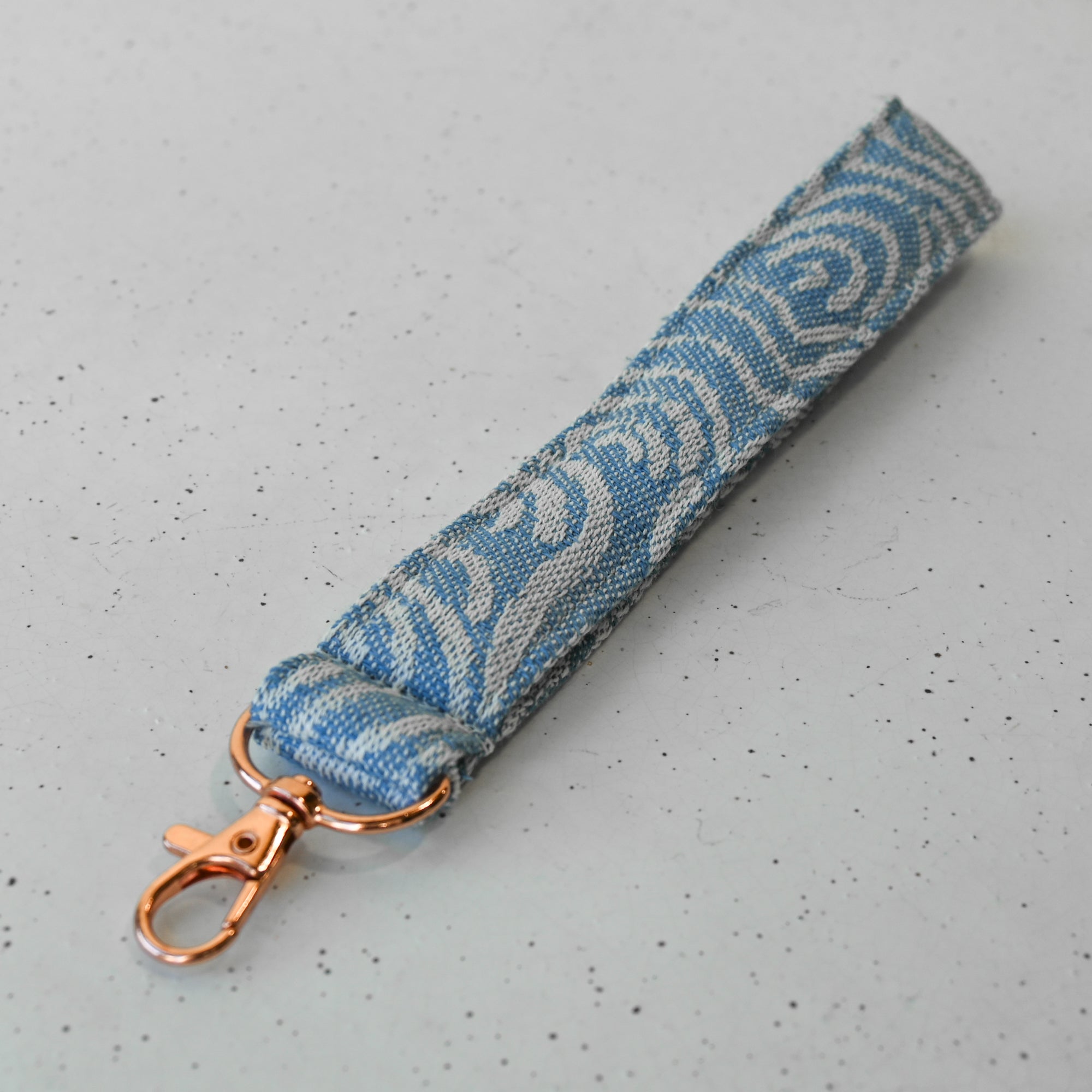 Blue and white patterned keychain strap with rose gold clasp on a white surface