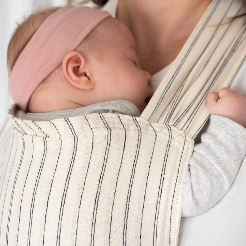 Newborn baby in a ink headband sleeping in a beige and gray striped baby carrier