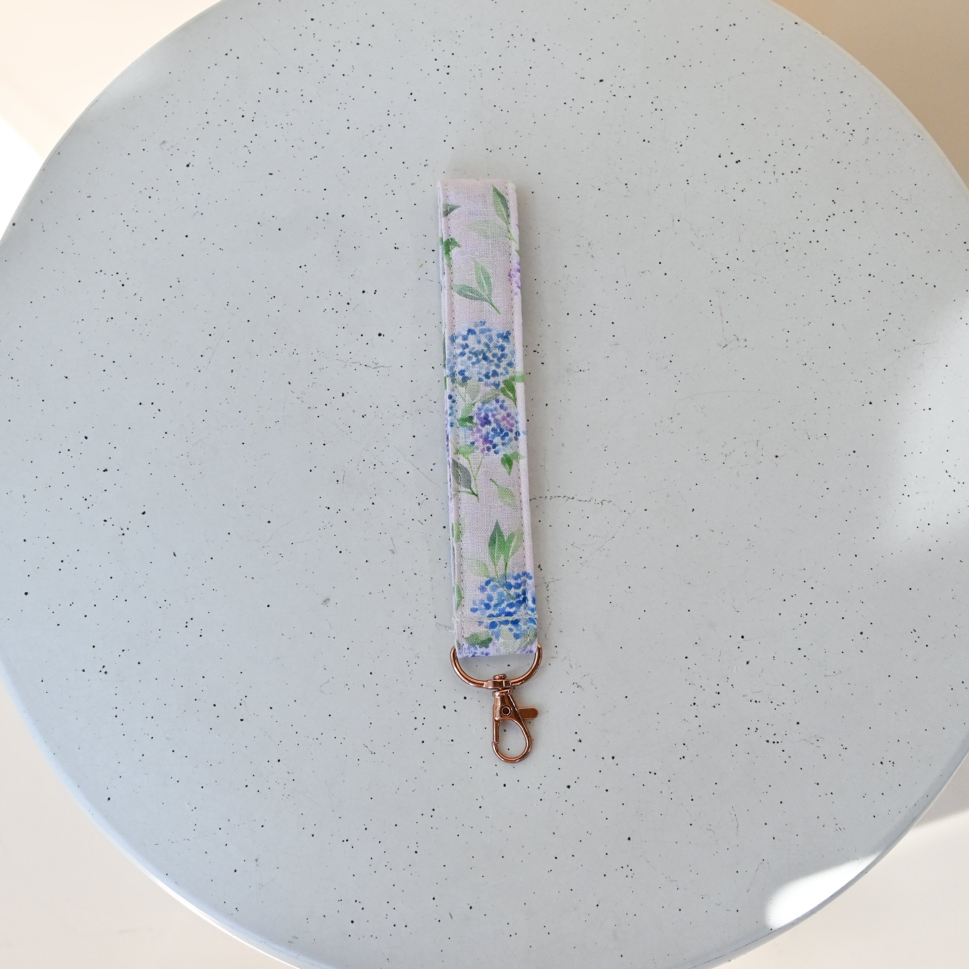 Key Fob in Blush — fabric wristlet strap with a rose-gold clasp, blue and lavender hydrangea print on a soft pink background.