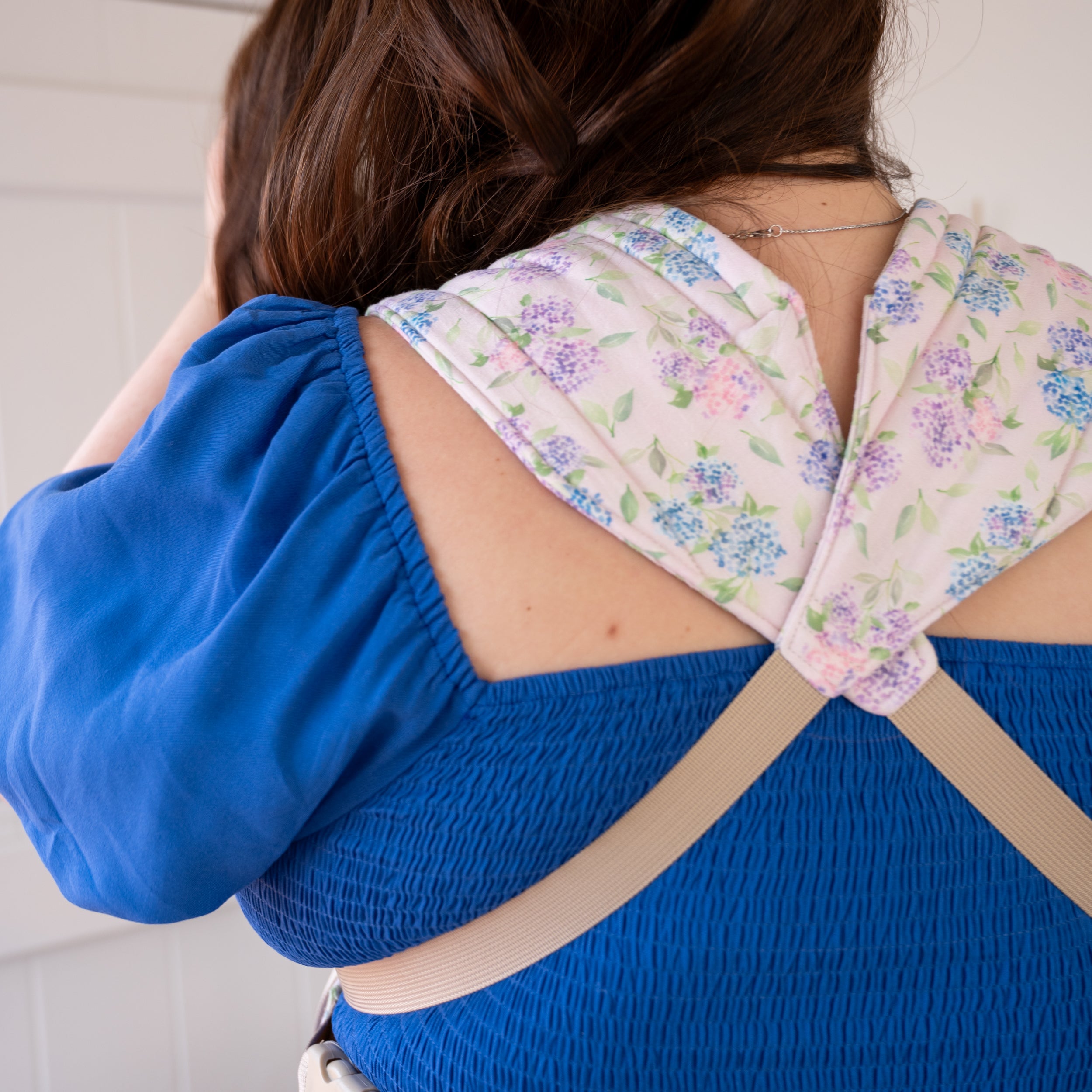 Lark Baby Carrier in Blush — close-up of the crossed padded shoulder straps in the blue and lavender hydrangea print on a soft pink background.