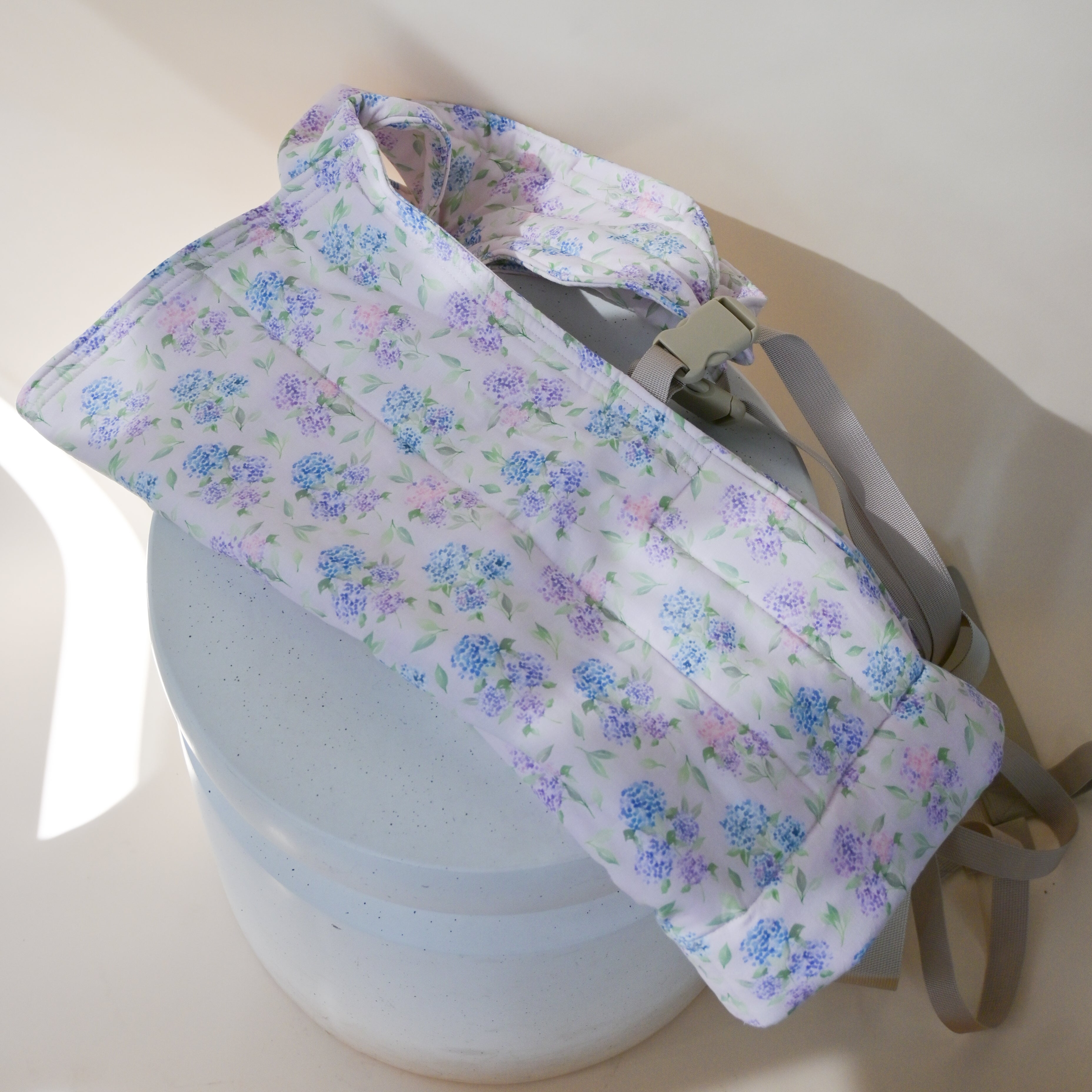 Lark Kid Carrier in Blush — the structured carrier shown unworn, quilted hydrangea-print panel in blue and lavender on a soft pink background.