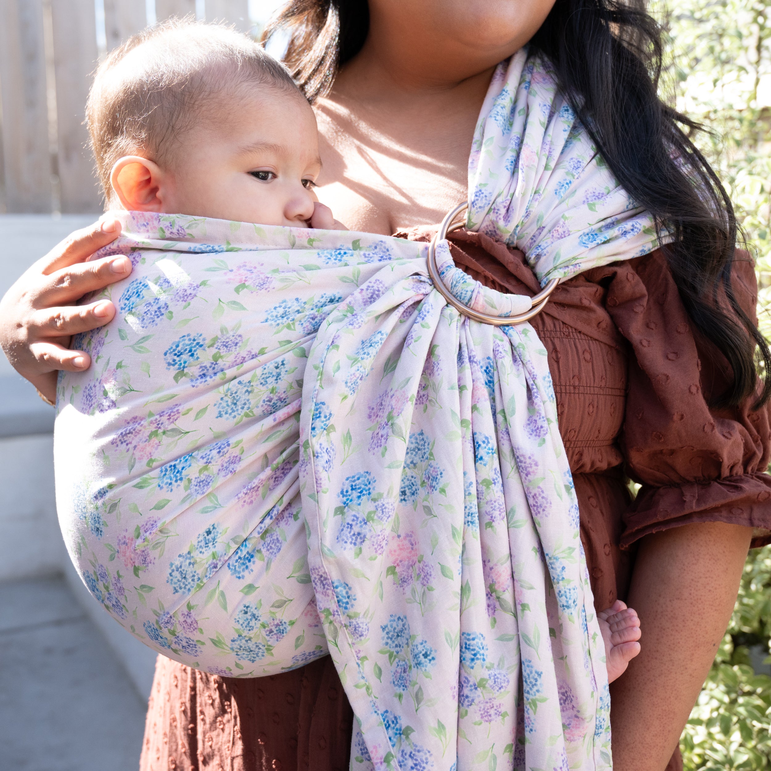 Ring Sling in Blush — baby nestled in the pouch beside the aluminium rings, blue and lavender hydrangea print on a soft pink background.