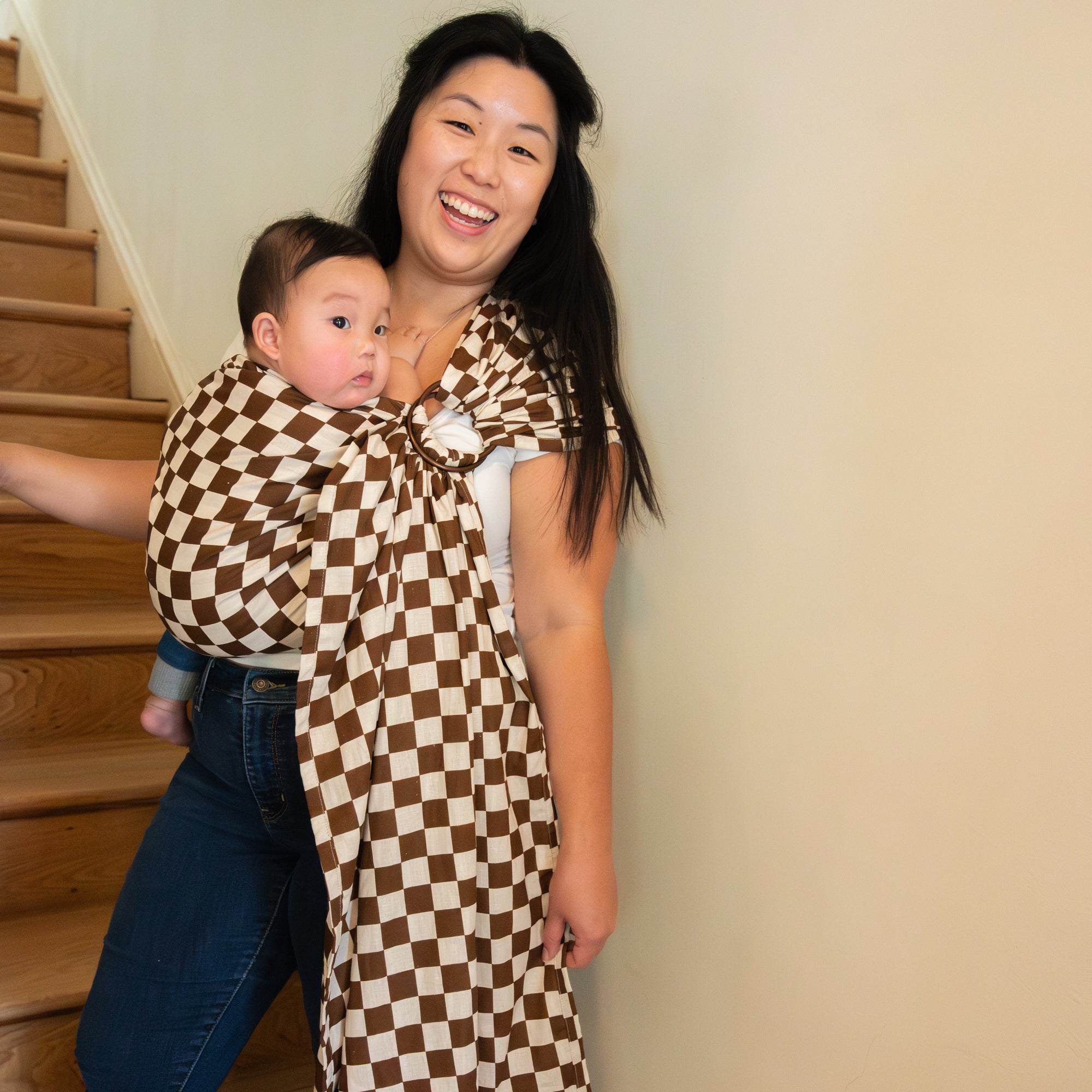 Woman carrying a baby in a checkered sling at home.