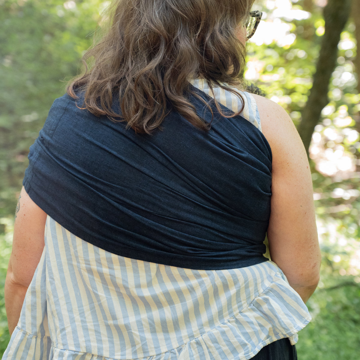 Back view of the Caspian Ring Sling spread smoothly across the wearer's shoulders and back in deep indigo woven chambray.