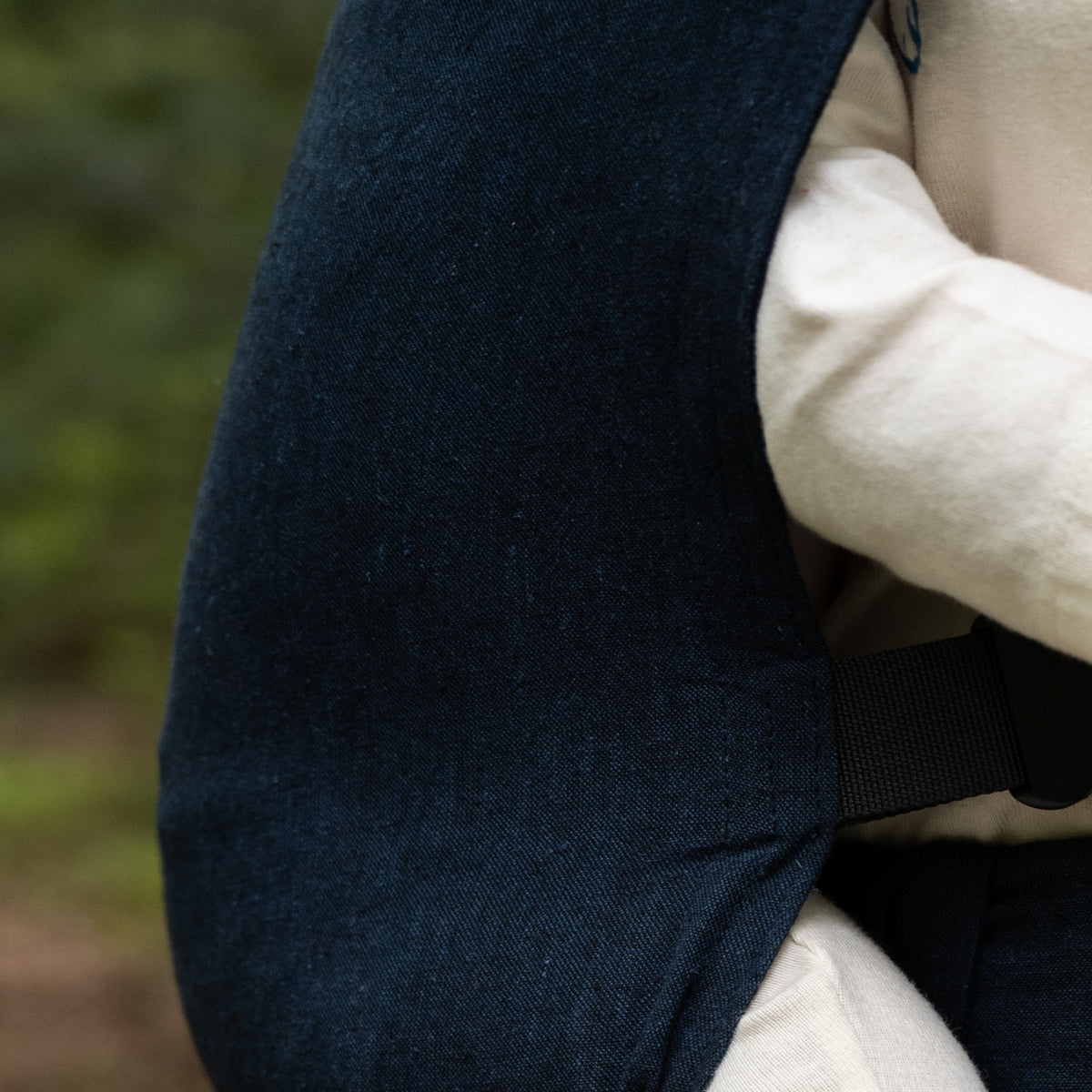 Close view of the Caspian Sprout Newborn Carrier's curved panel edge and black webbing strap, showing the deep indigo woven chambray.