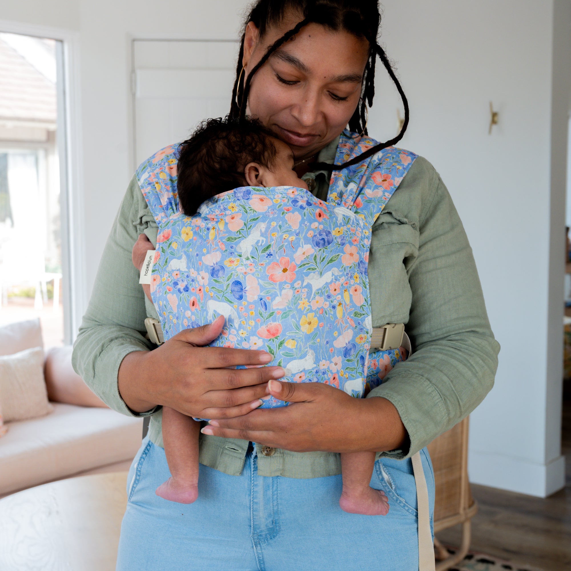 Woman carrying a baby in a floral unicorn patterned carrier.