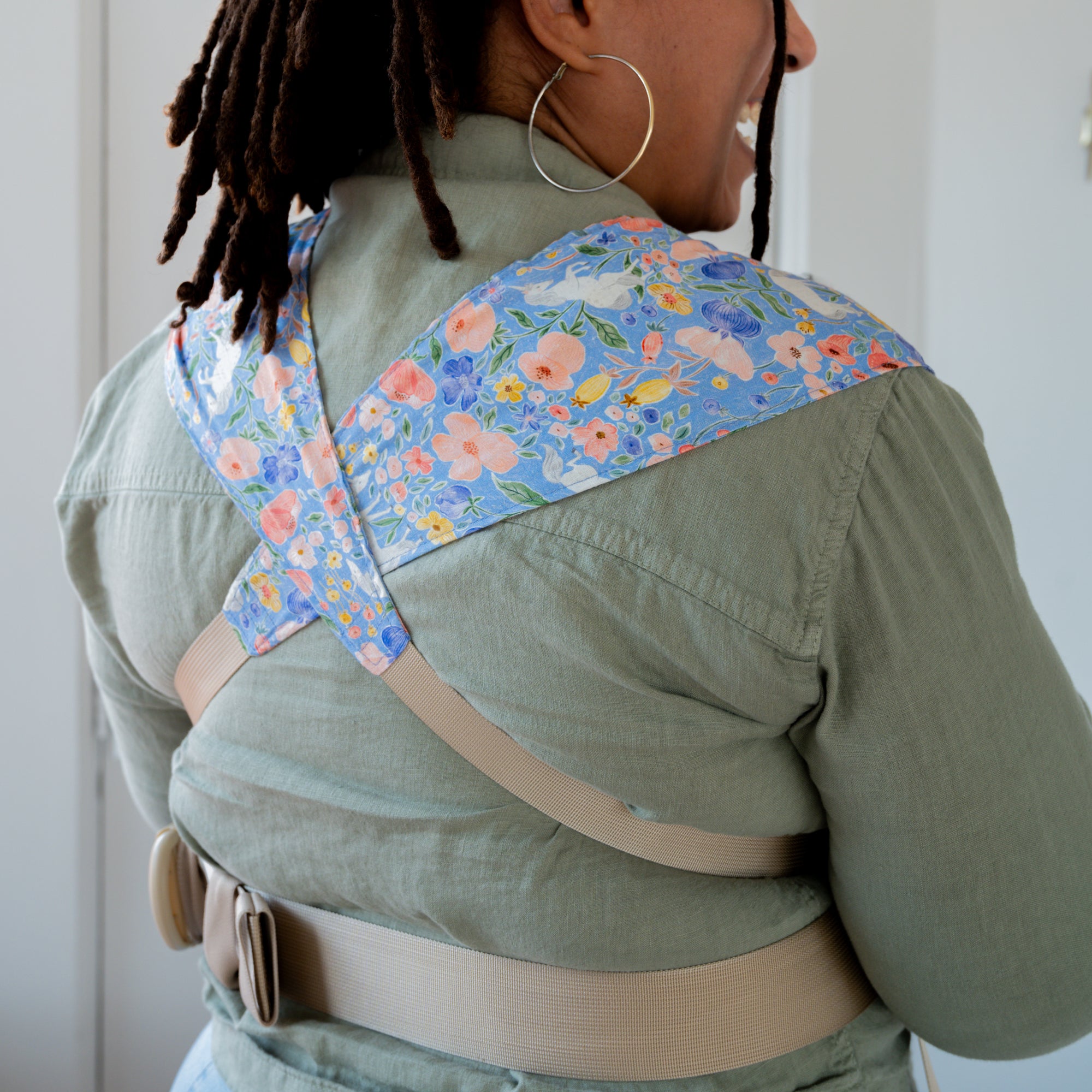 Woman carrying a baby in a floral unicorn patterned carrier.