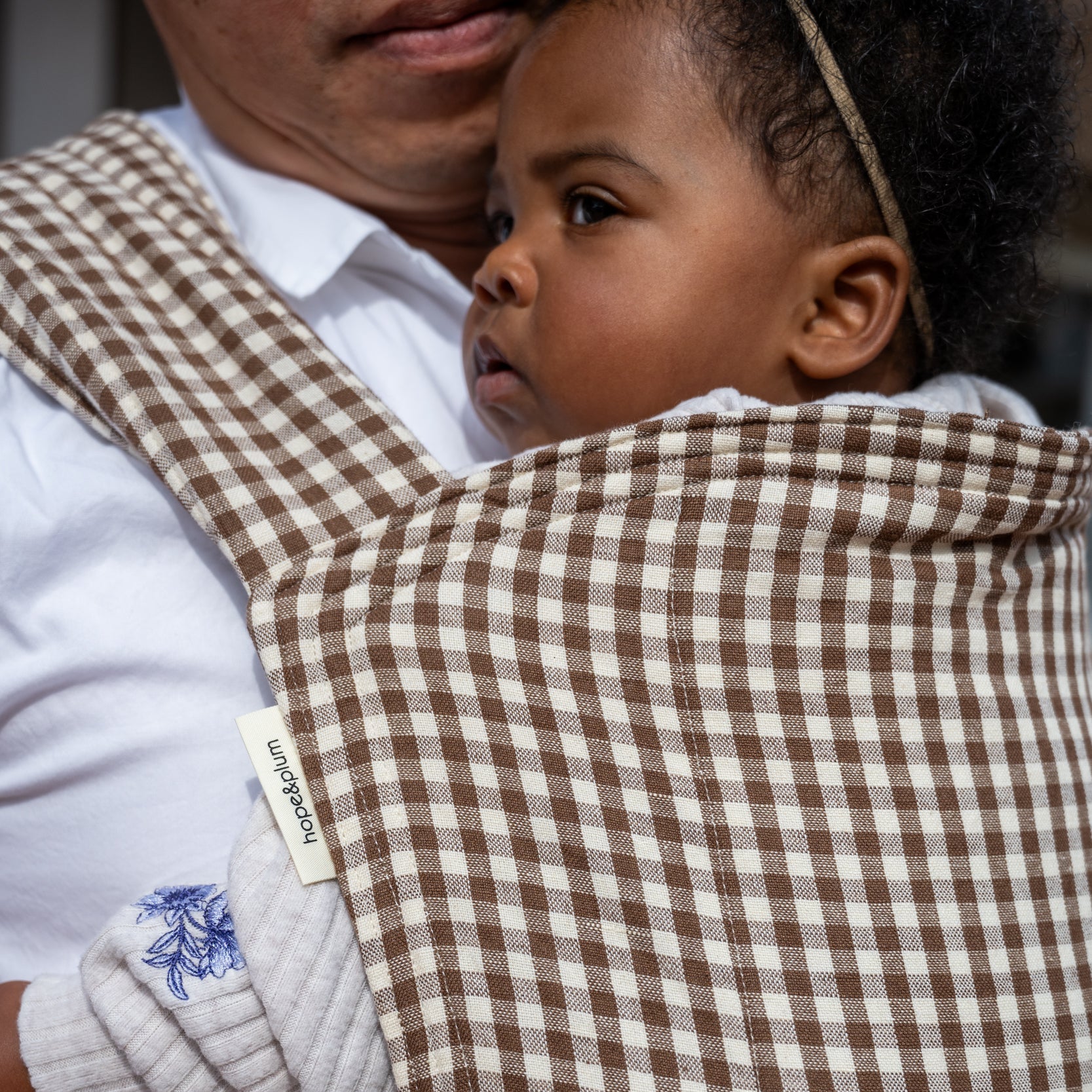 Lark Baby Carrier in Clove — close-up of the gingham quilted hood against a caregiver's shoulder, toddler peeking out.