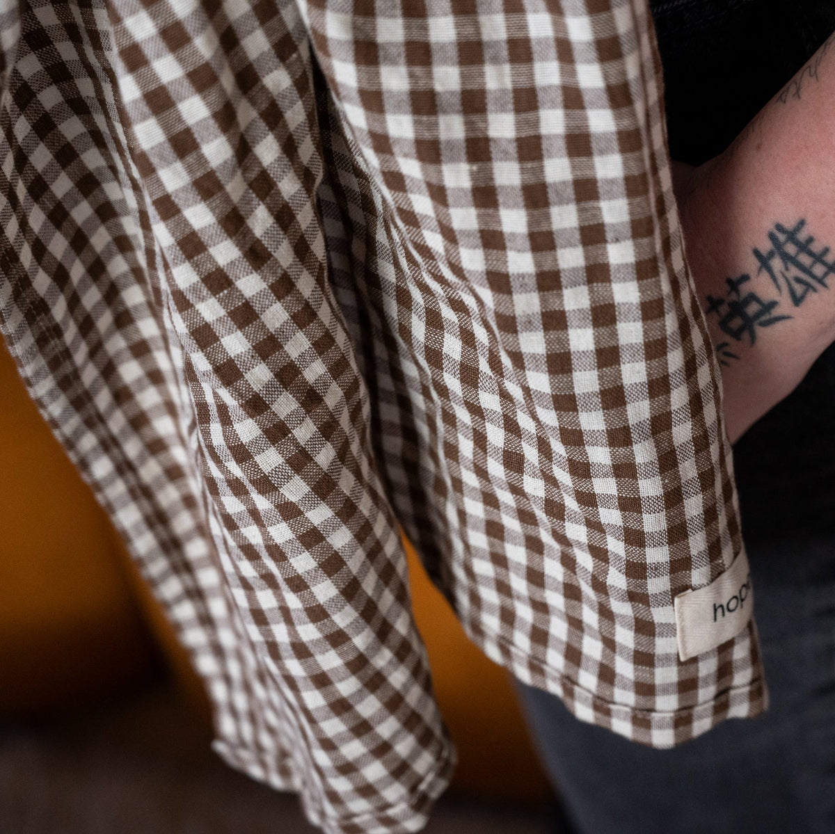 Ring Sling in Clove — close-up of the gingham cuff and label, caregiver's forearm tattoo visible.