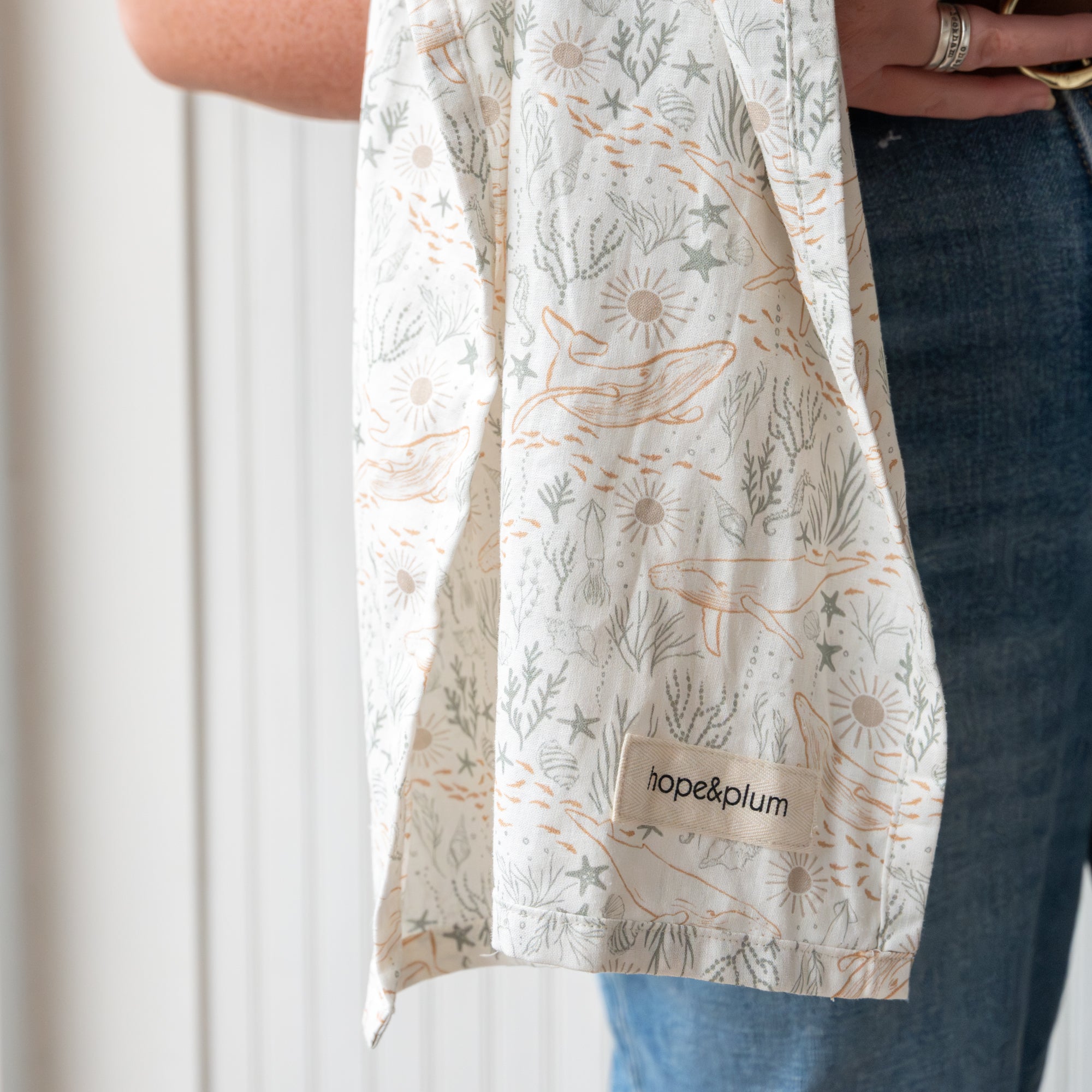 An ocean print baby ring sling against a white wall.