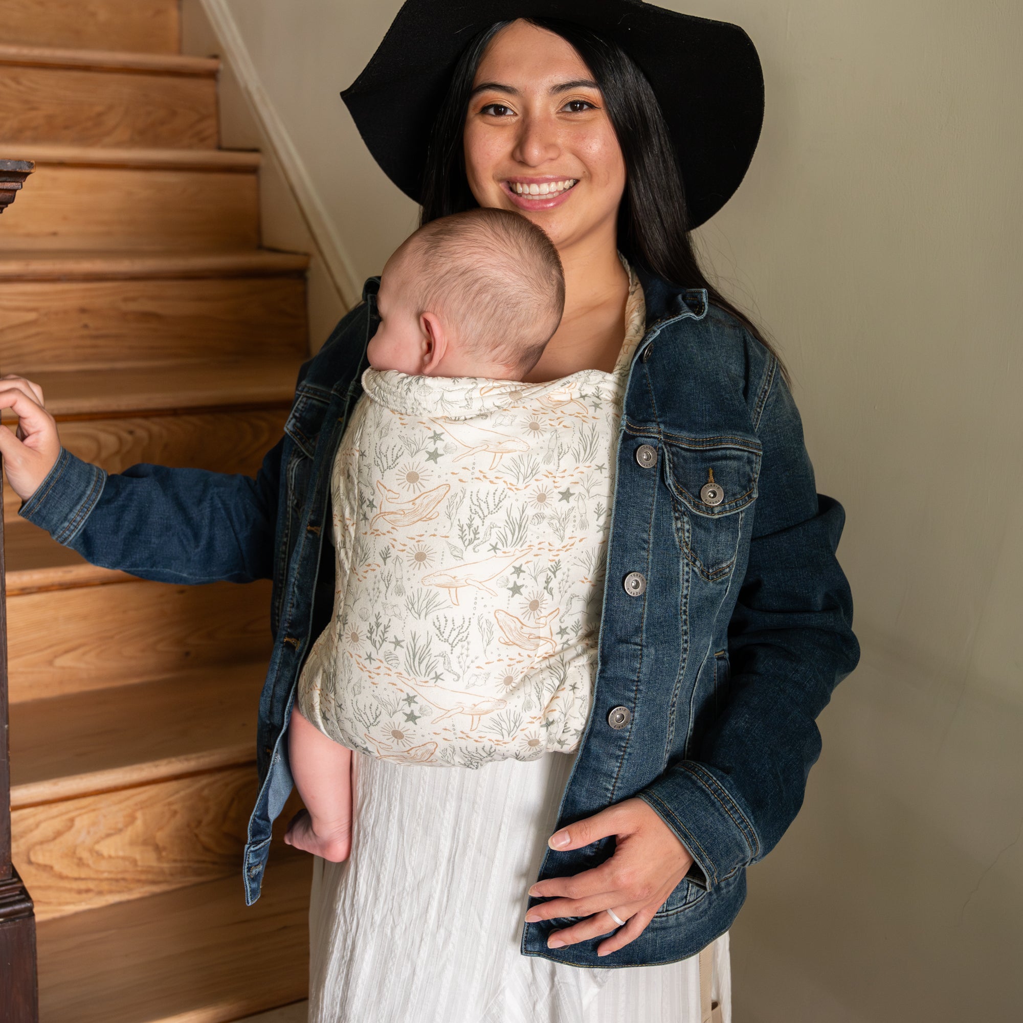 Baby in a ocean-themed baby carrier held by a person in a denim jacket.