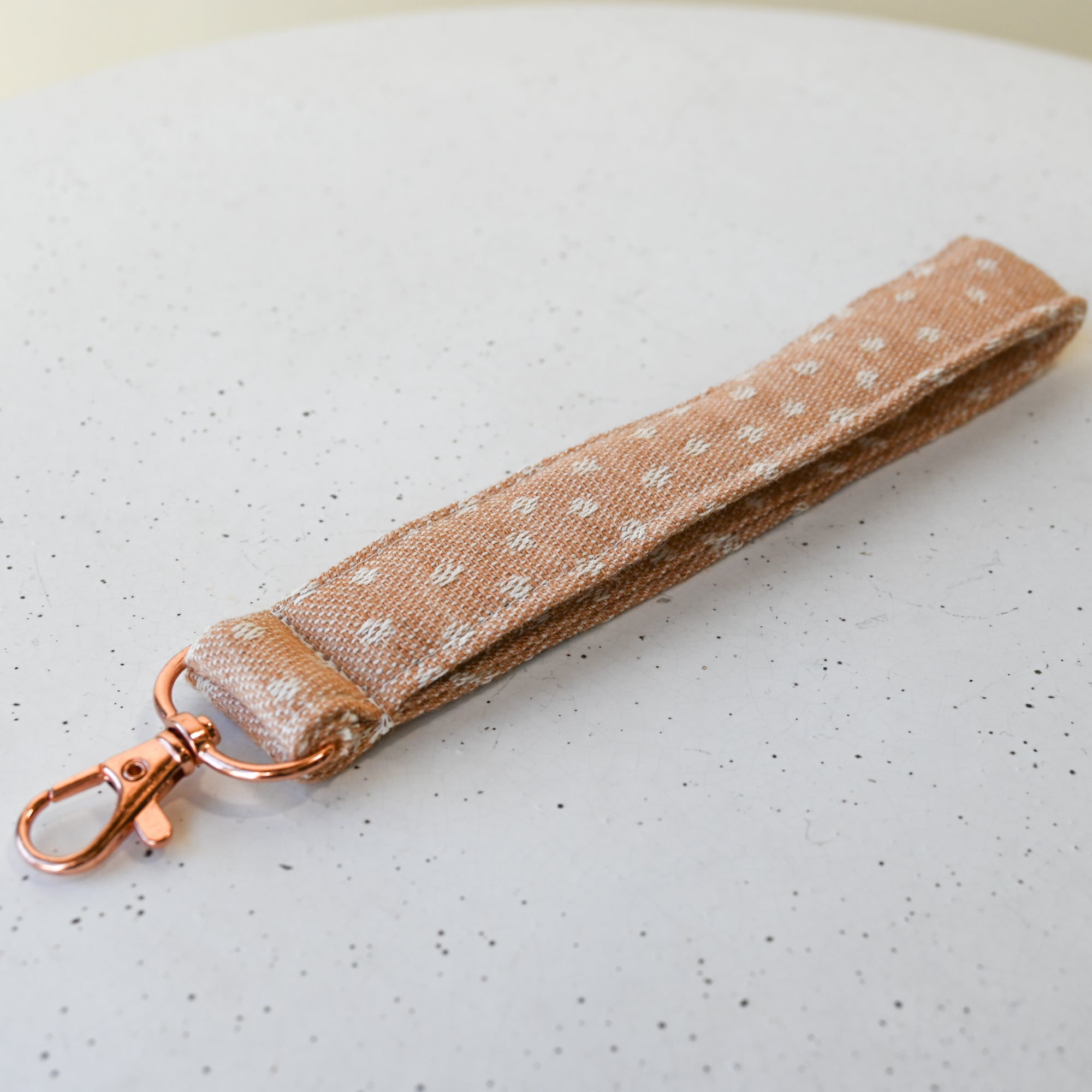 Beige keychain strap with white polka dots on a white surface