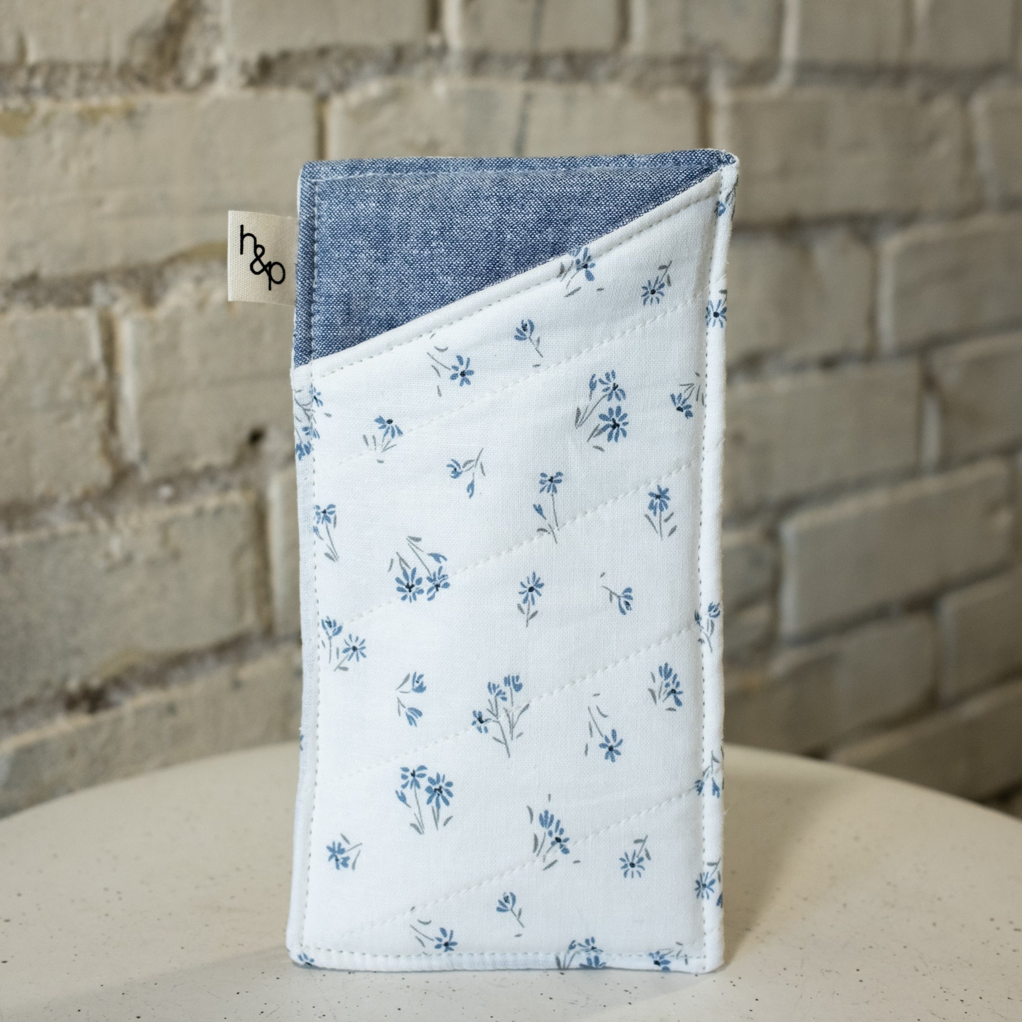 Fabric pouch with floral pattern on a white surface with brick wall background