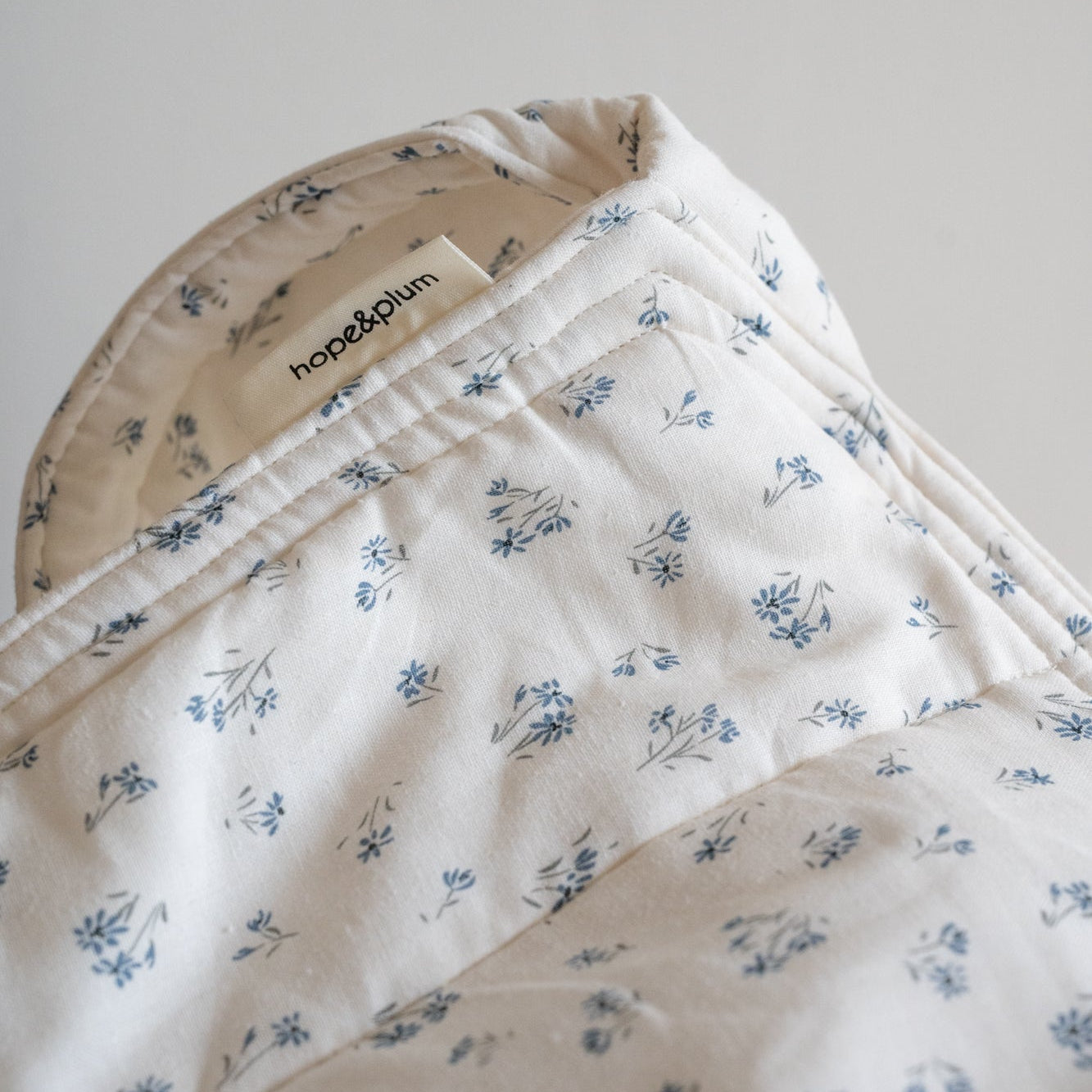 Floral-patterned baby carrier with 'hope&plum' label on a light gray background