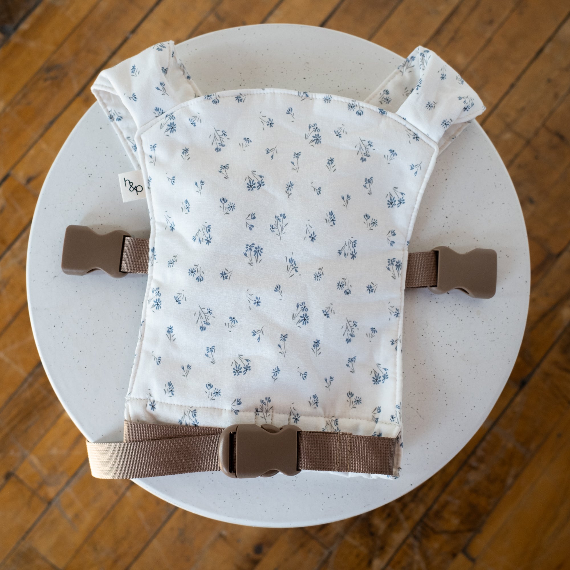 doll carrier with floral pattern and brown straps on a white surface.