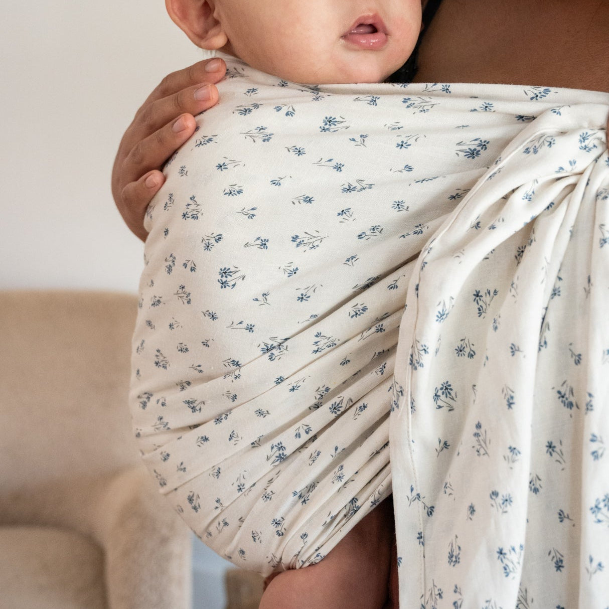 Woman holding a baby wrapped in a floral-patterned ring sling.