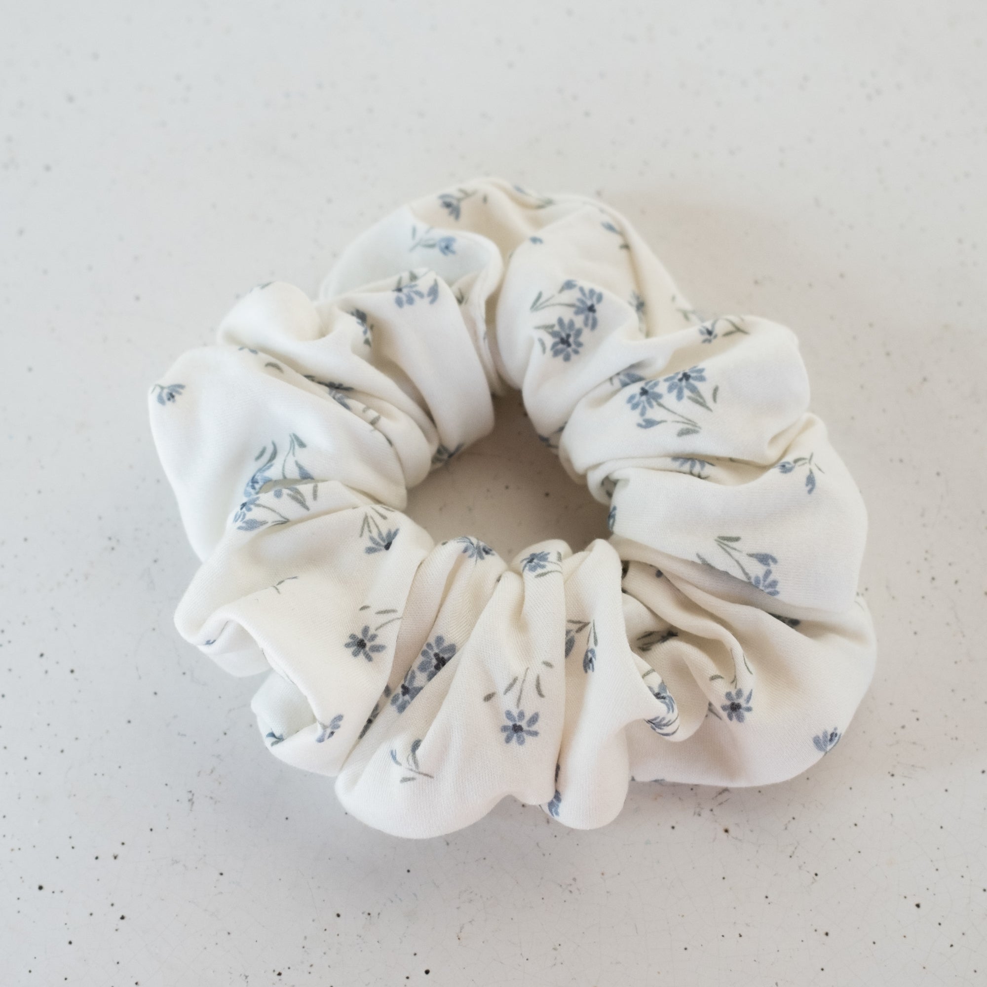White scrunchie with blue floral pattern on a light gray background