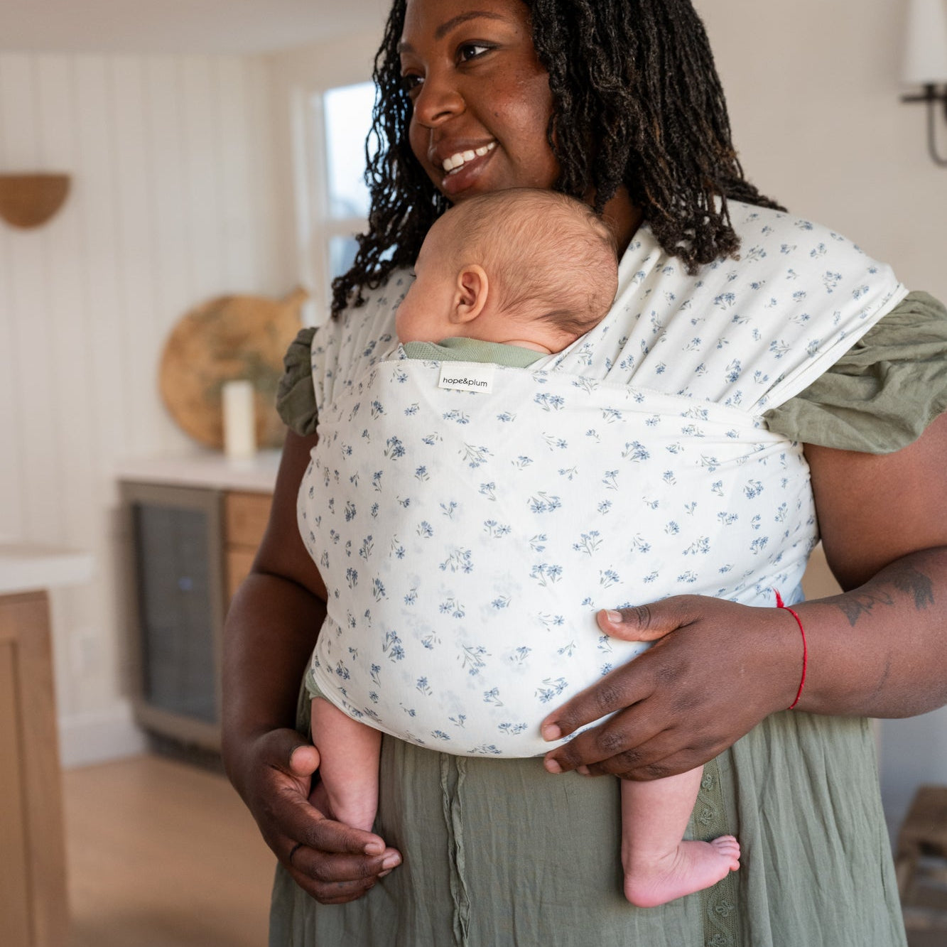 Woman holding a baby in a dainty floral wrap in a home setting