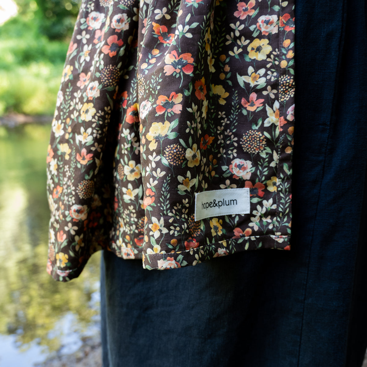 Close-up of the Ember Ring Sling's tail and hope&plum label, a rich, chocolate brown hemp-cotton fabric printed with autumnal watercolor florals.